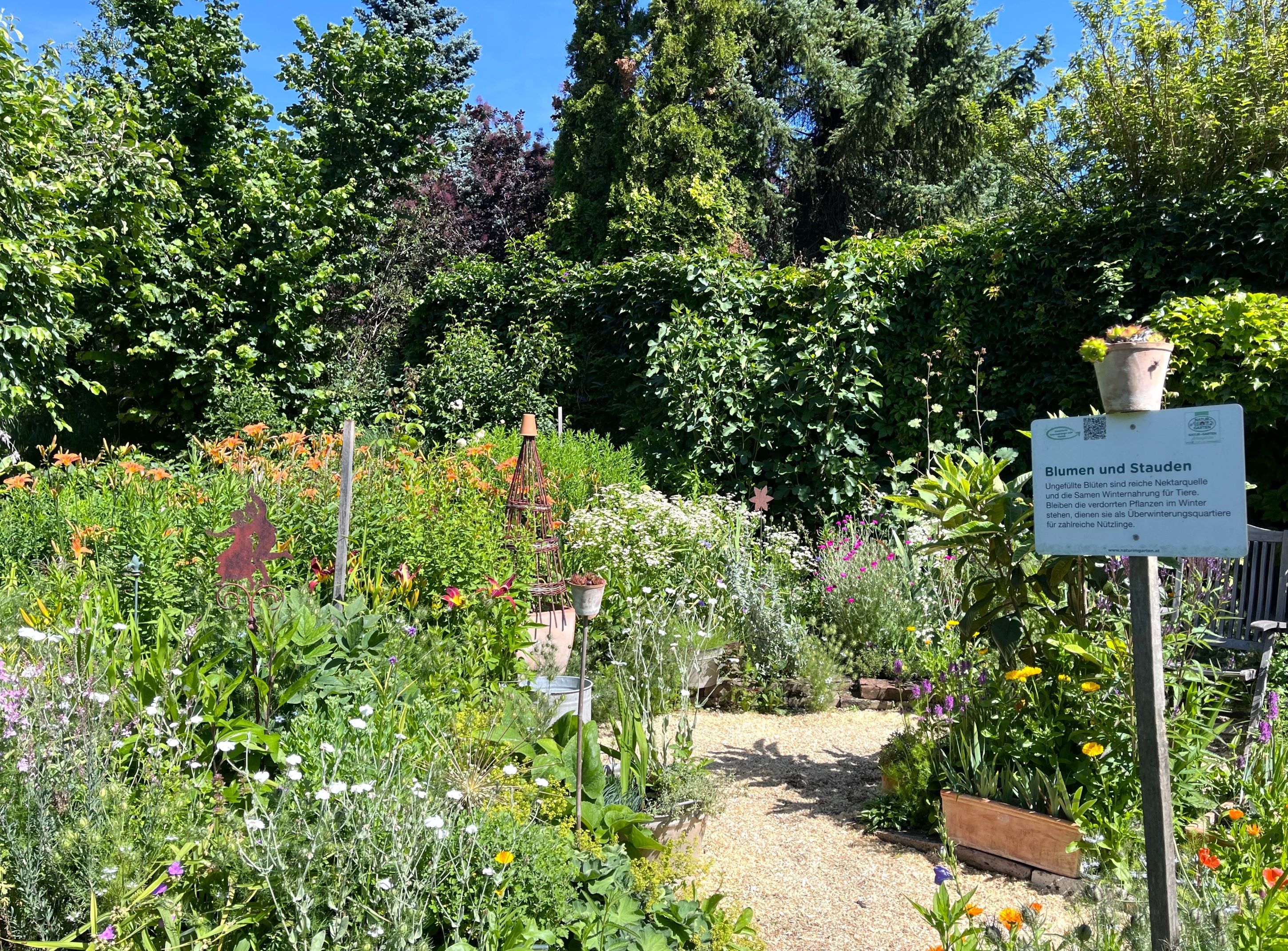 Ein bunter Bauerngarten mit verschiedenen Blumen und einem Schild, das "Blumen und Stauden" beschreibt.