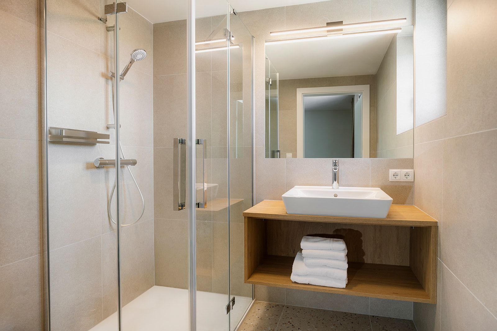 Modernes Badezimmer mit Glasdusche und Waschbecken auf Holzablage.