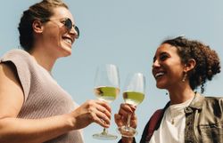 Zwei Freundinnen stoßen mit Gläsern voll erfrischendem Wein an und genießen die strahlende Sonne. Umgeben von sanften Hügeln und üppigen Weinreben, strahlt die Atmosphäre Freude und Entspannung aus. Der Weinherbst lädt dazu ein, die köstlichen Aromen der Region zu entdecken.