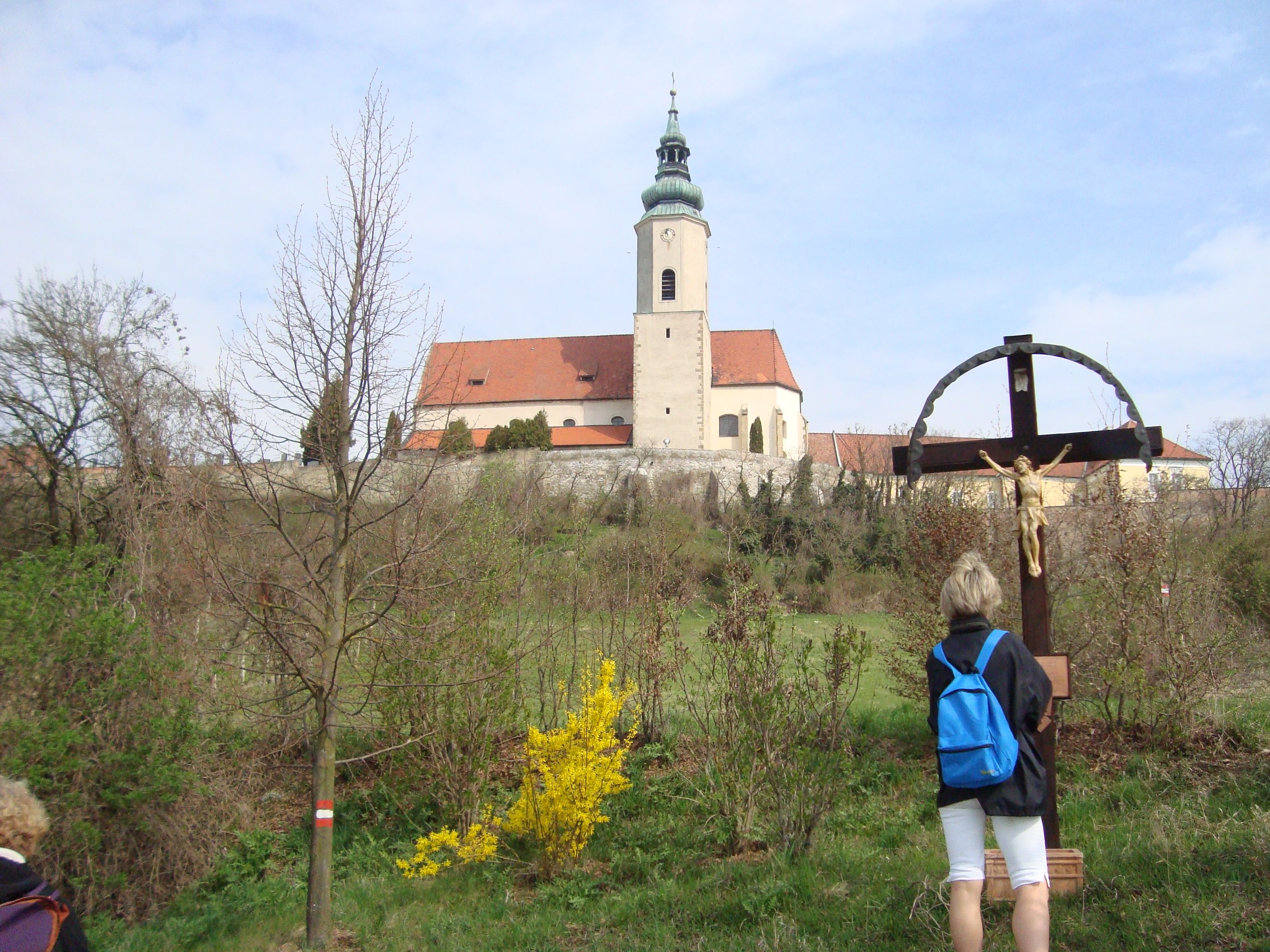 Eine Kirche auf einem Hügel mit einem Kreuz im Vordergrund und einer Person, die das Kreuz betrachtet.