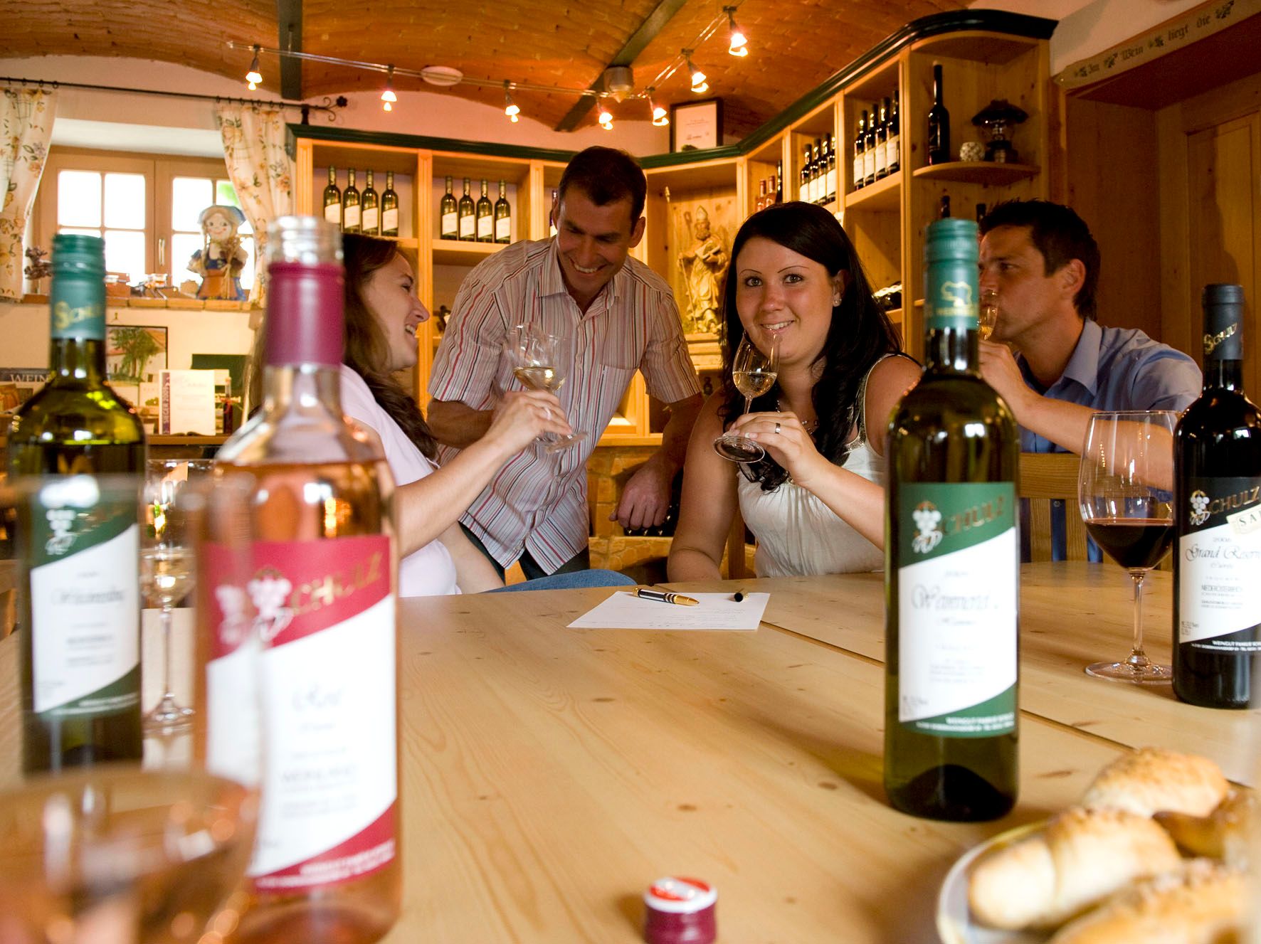 Group of people at a wine tasting in a cozy room with bottles of wine on the table.