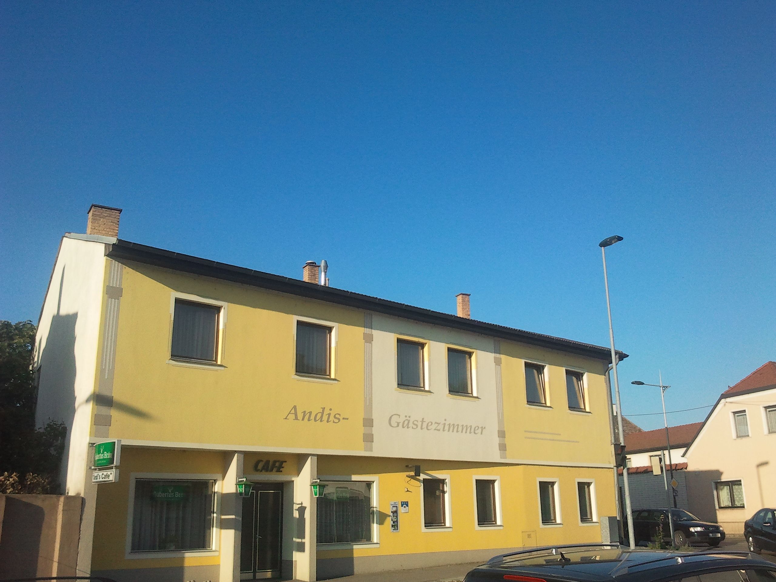 Gelbes Gebäude mit der Aufschrift 'Andis Gästezimmer' und 'Cafe'.