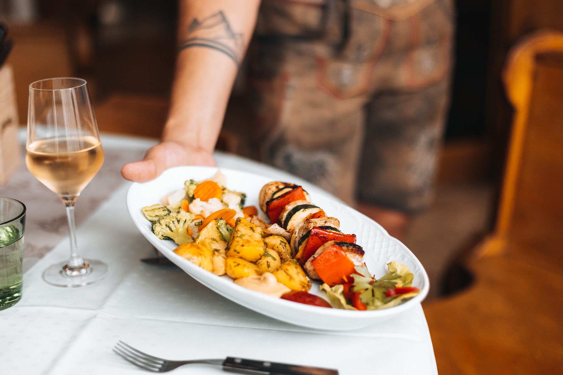 Ein köstlicher Teller mit gegrilltem Gemüse und bunten Spießen wird liebevoll serviert, während ein Glas Weißwein die Atmosphäre perfekt abrundet. Die rustikale Umgebung des Gasthofs lädt dazu ein, die regionalen Spezialitäten in vollen Zügen zu genießen und die Seele baumeln zu lassen.