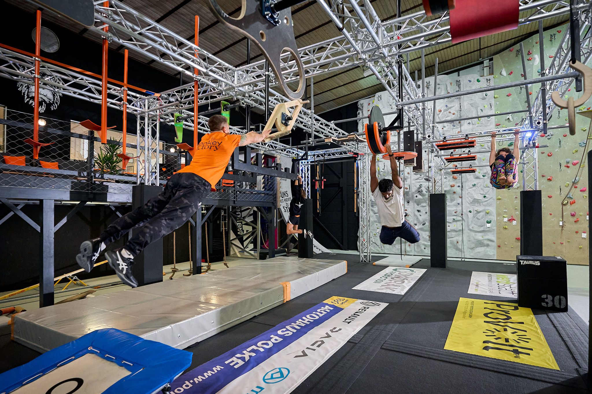 People train in an indoor climbing park with various obstacles and climbing walls.