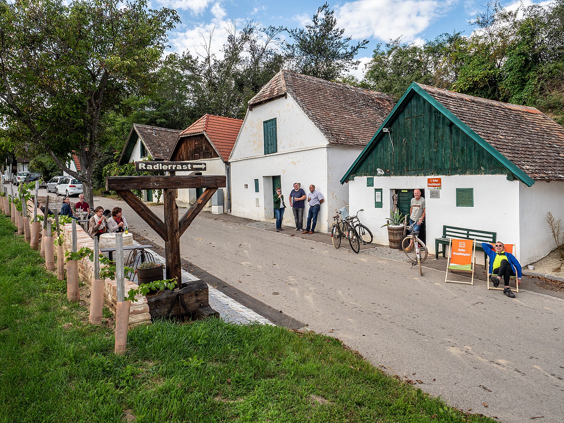 Weinkellerstraße in Mailberg mit Menschen, Fahrrädern und einem Schild 'Radlerrast'.