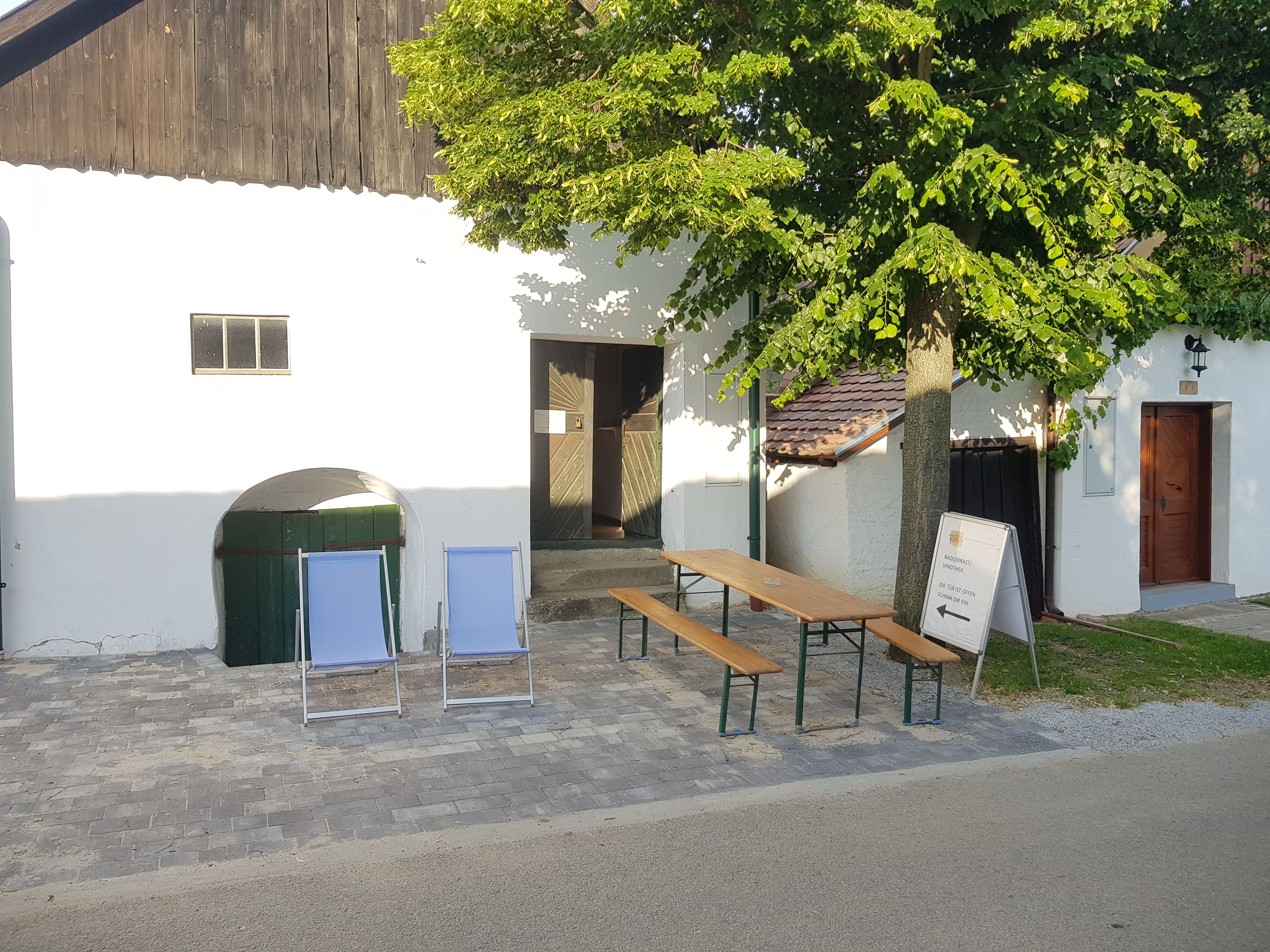 Zwei Liegestühle und ein Tisch mit Bänken vor einem weißen Gebäude mit Baum.