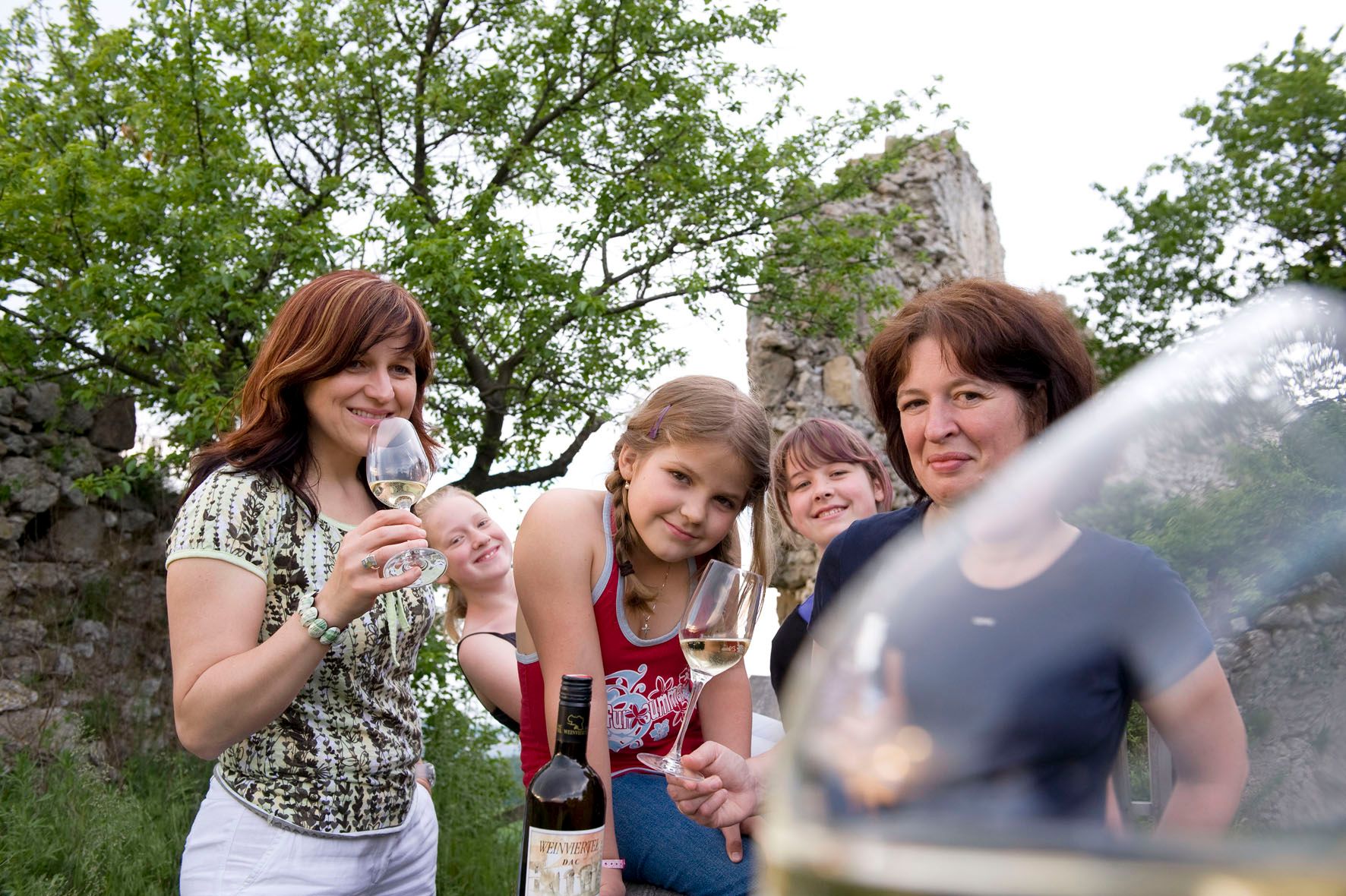 Group of people outdoors with wine glasses and wine bottle.