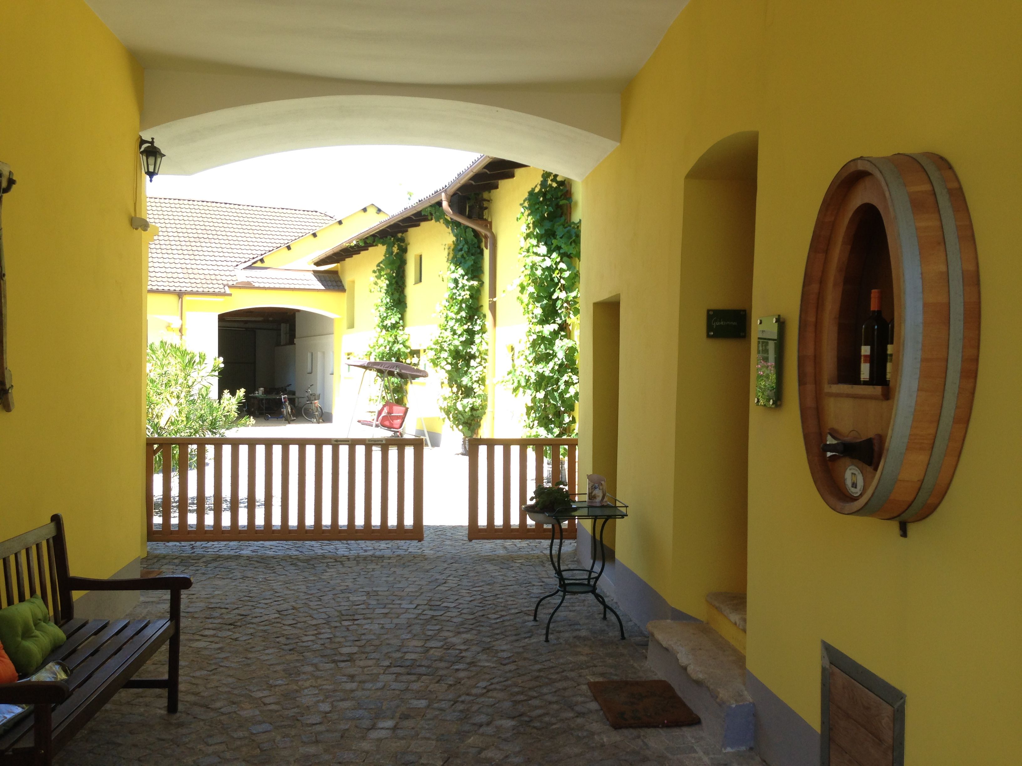 Innenhof eines gelben Gebäudes mit Weinfass-Dekoration und Holztor.
