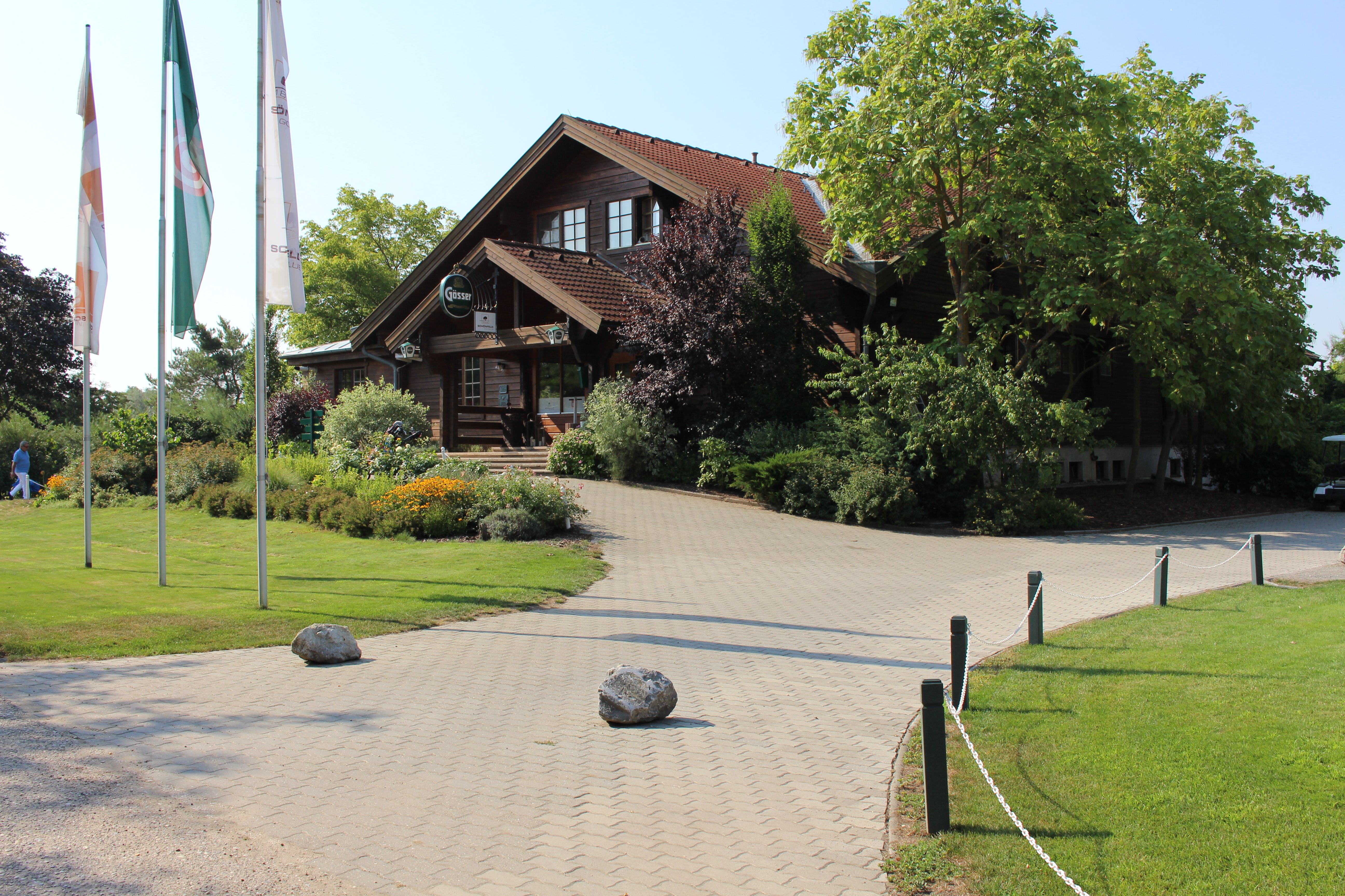 Entrance of a golf club with wooden building and flags.