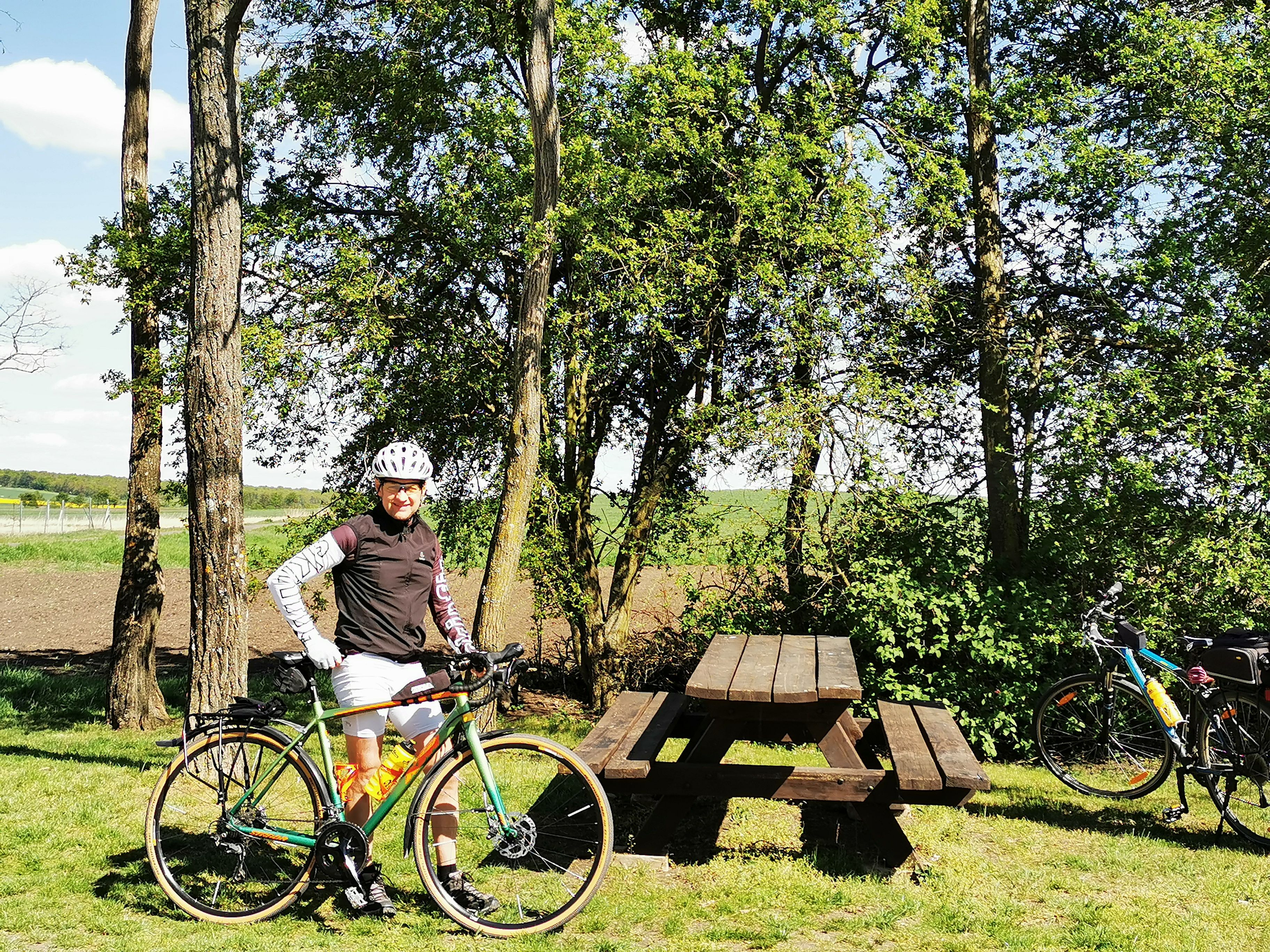 Person mit Fahrrad neben Picknicktisch im Grünen.