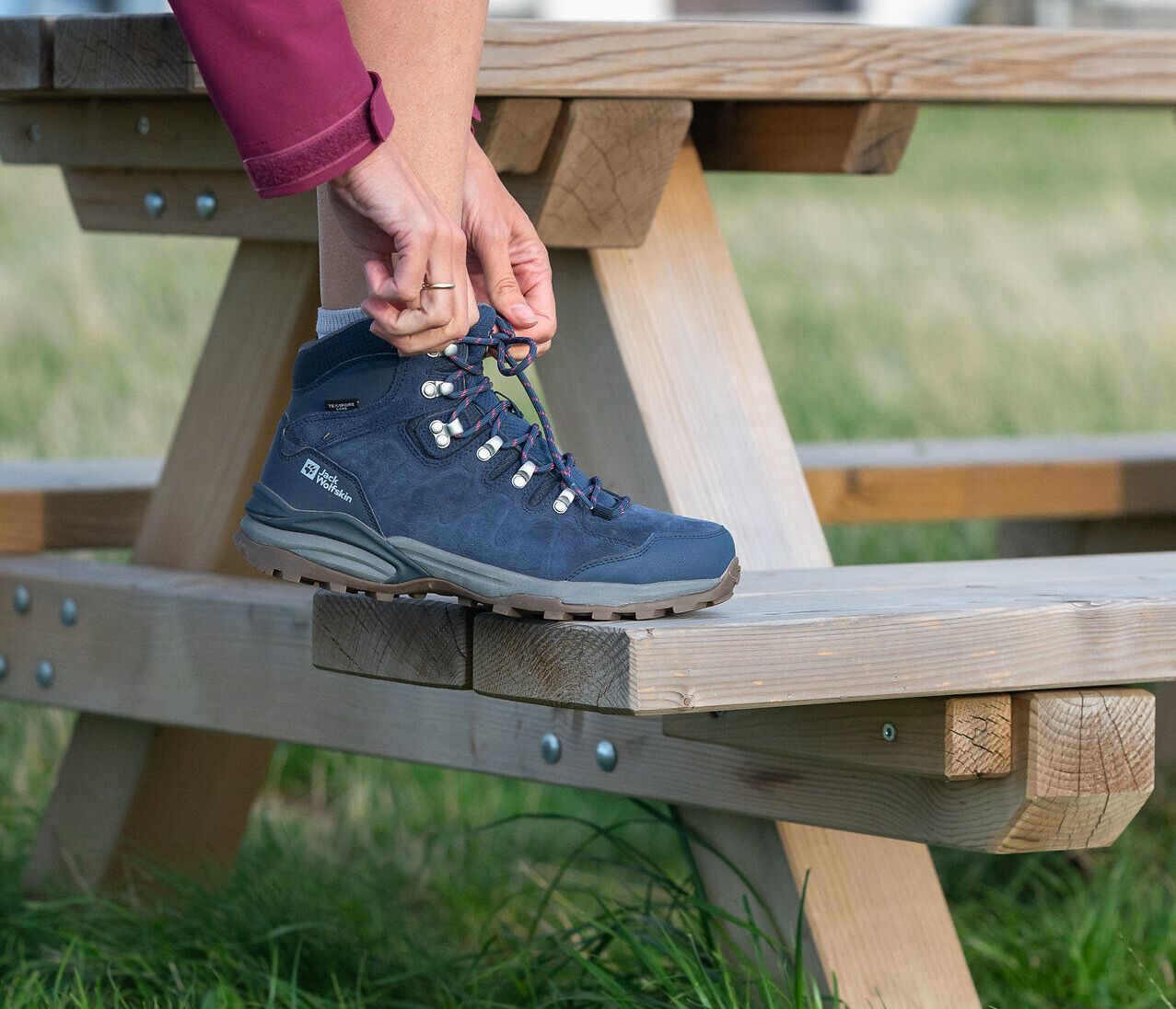 Eine Person hat den Fuß auf einer Holzbank abgestellt und schnürt den Wanderschuh zu.