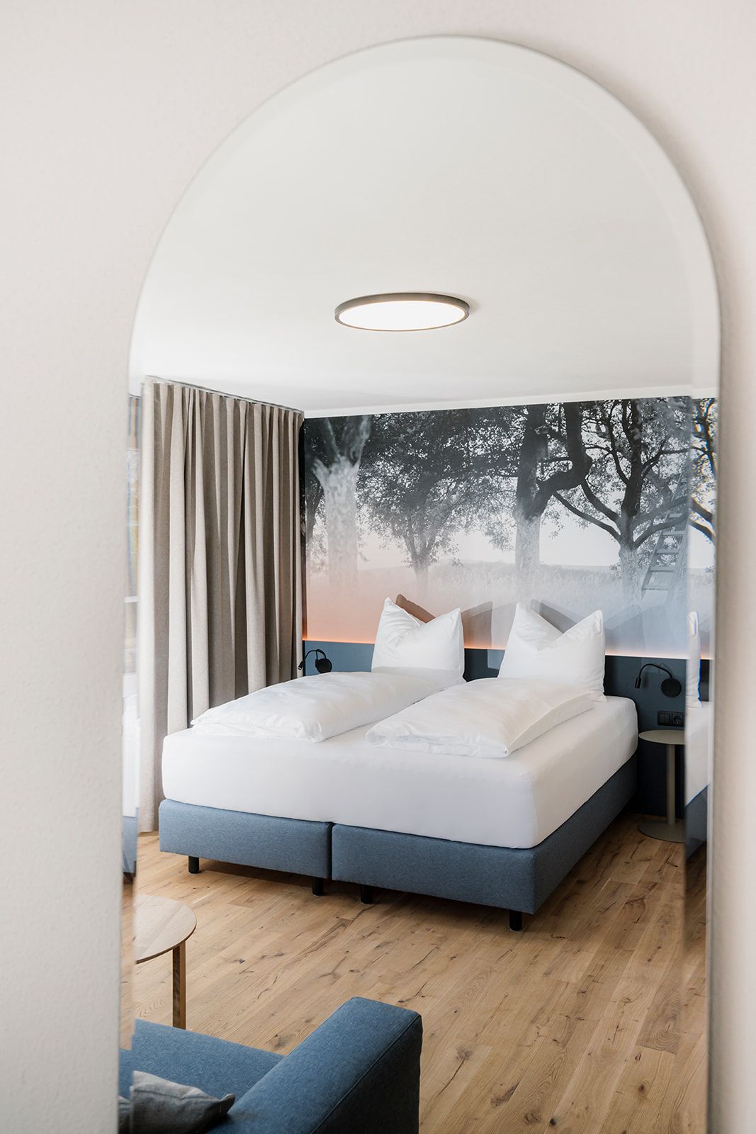 Modernes Hotelzimmer mit Doppelbett, Holzboden und Wandbild von Bäumen.