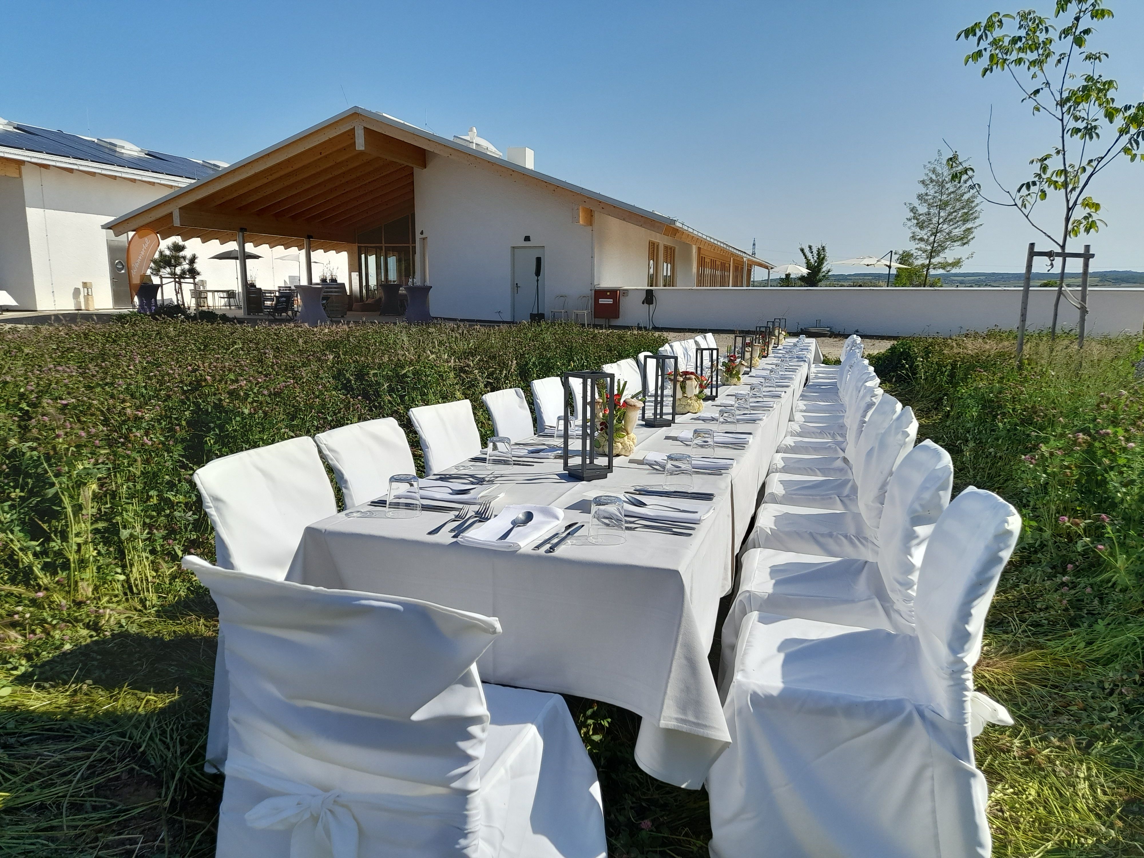 Langer, gedeckter Tisch im Freien vor einem modernen Gebäude mit Holzveranda.