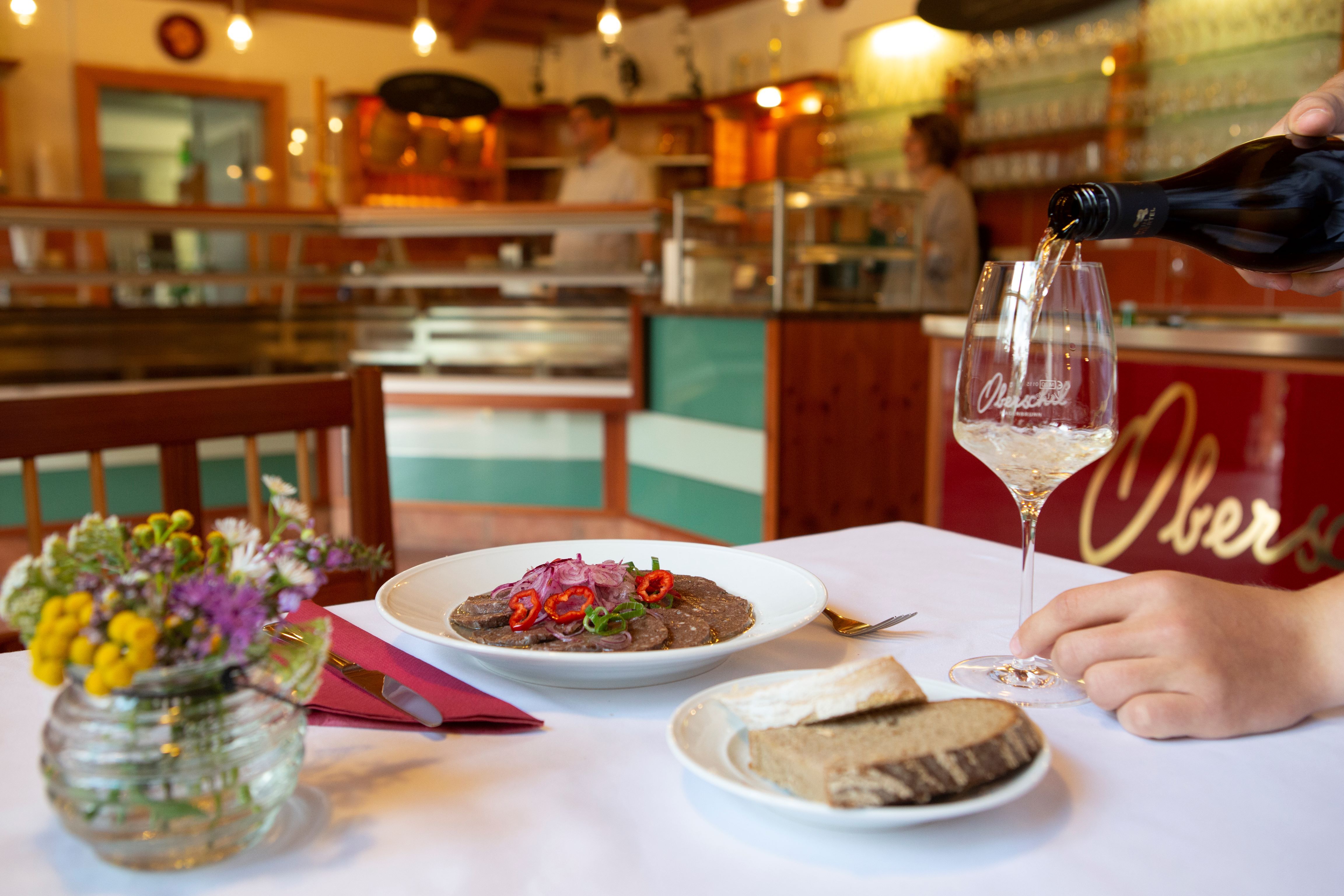 Ein gedeckter Tisch in einem Heurigenlokal mit einem Teller Essen, Brot und einem Glas Wein.