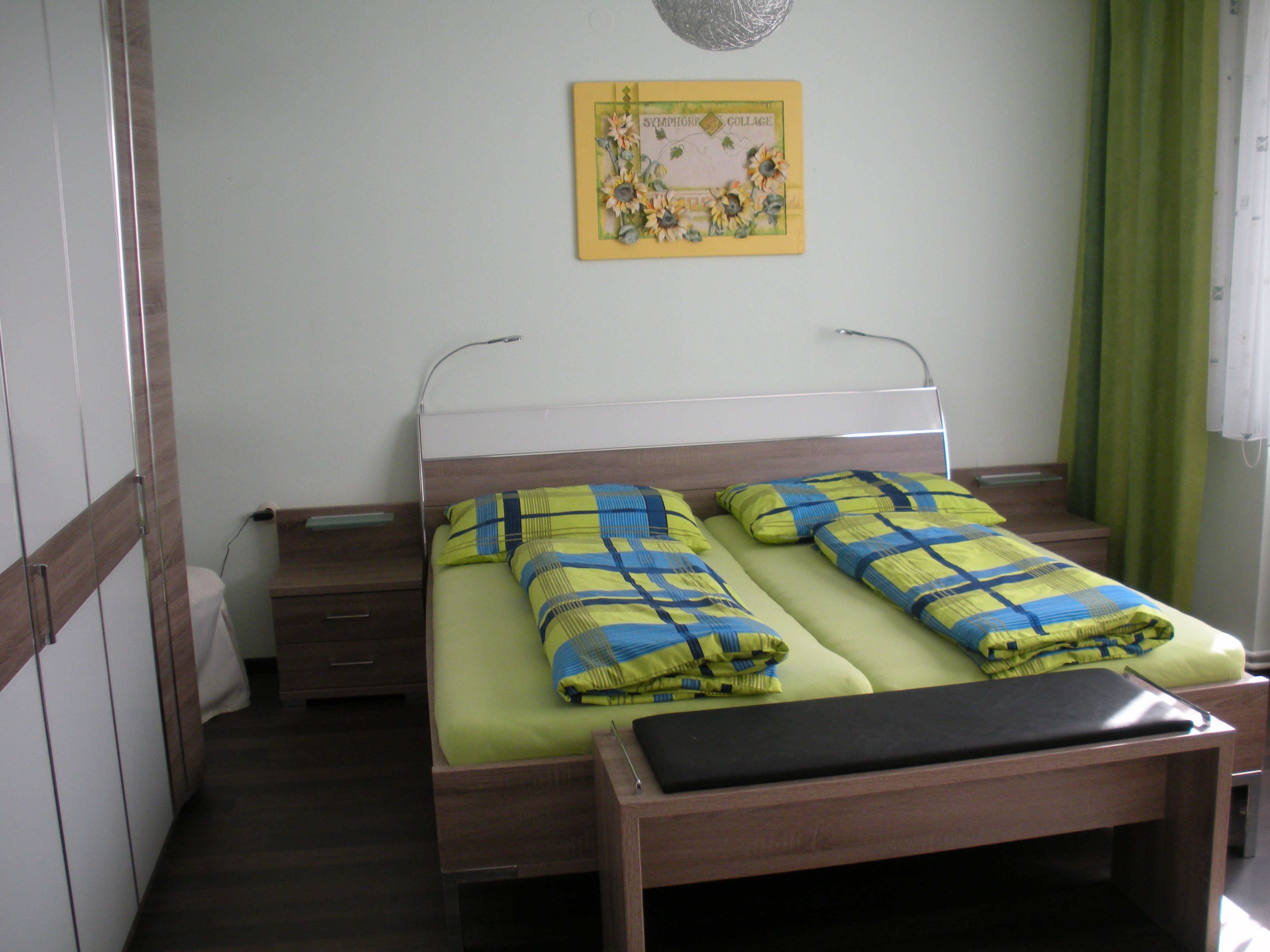 Gästezimmer mit Doppelbett, bunter Bettwäsche und Wandbild.