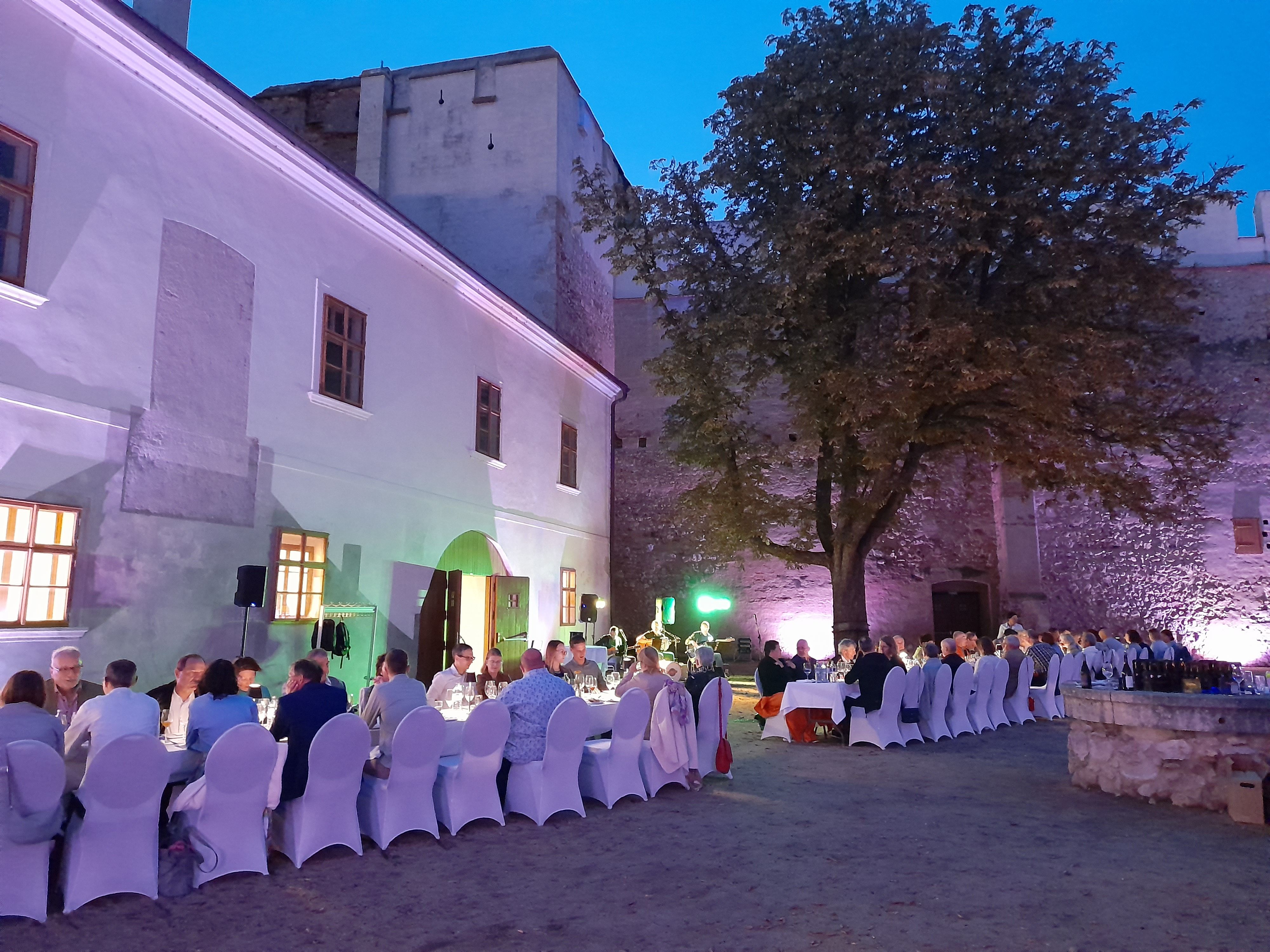 Abendessen im Freien mit langen Tischen und Stühlen in einem historischen Innenhof.