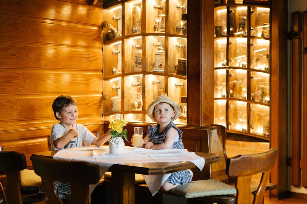 Dvě děti sedí u stolu v dřevem obložené restauraci.