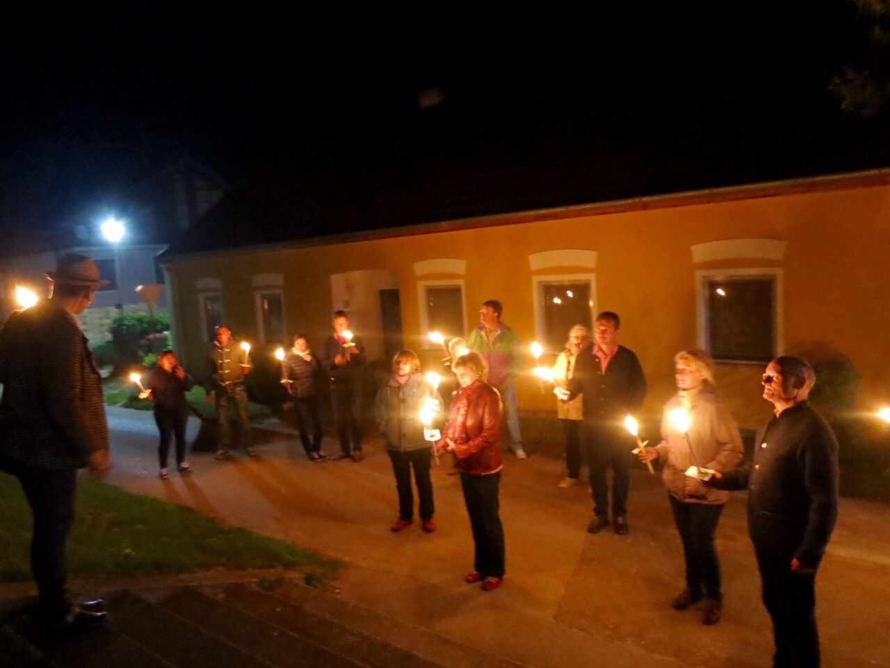 Menschen stehen nachts mit Fackeln vor einem gelben Gebäude.