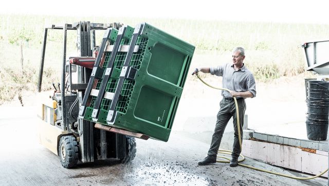 Ein Mann reinigt mit einem Wasserschlauch eine große grüne Kiste, die von einem Gabelstapler gehalten wird.