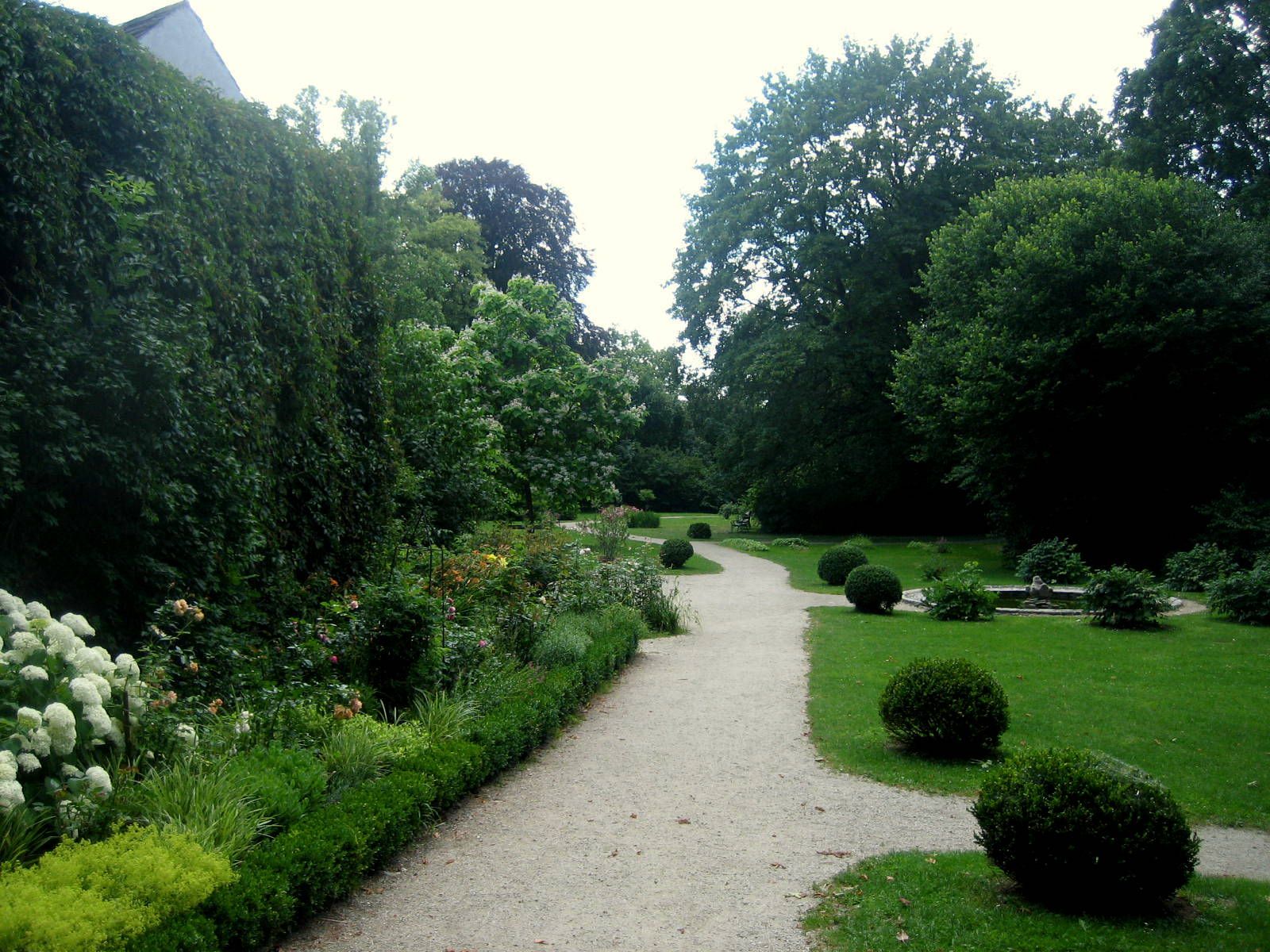 Ein gepflegter Gartenweg im Schlosspark Mühlbach, umgeben von Büschen und Bäumen.