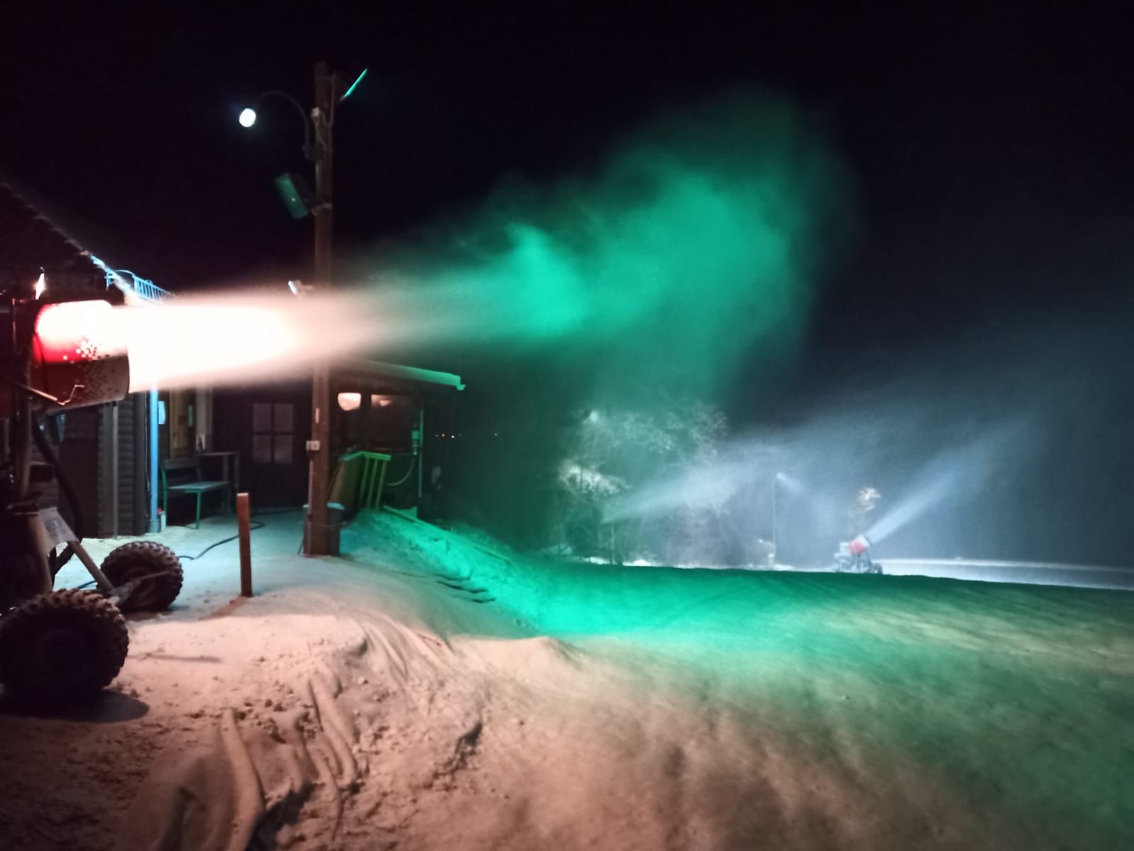 Schneekanone bei Nacht mit grünem Licht beleuchtet.