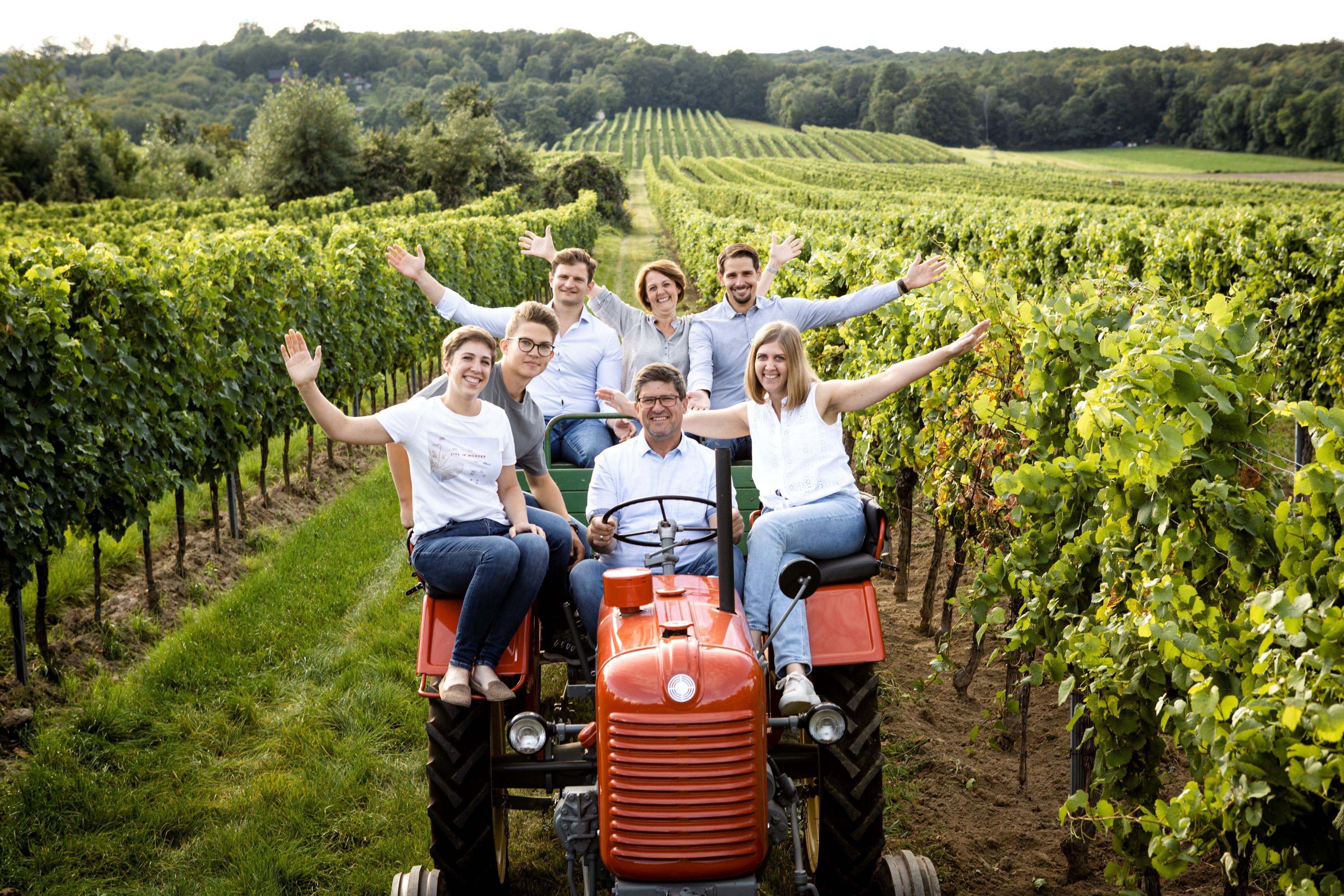 Gruppe von Menschen auf einem Traktor in einem Weinberg.