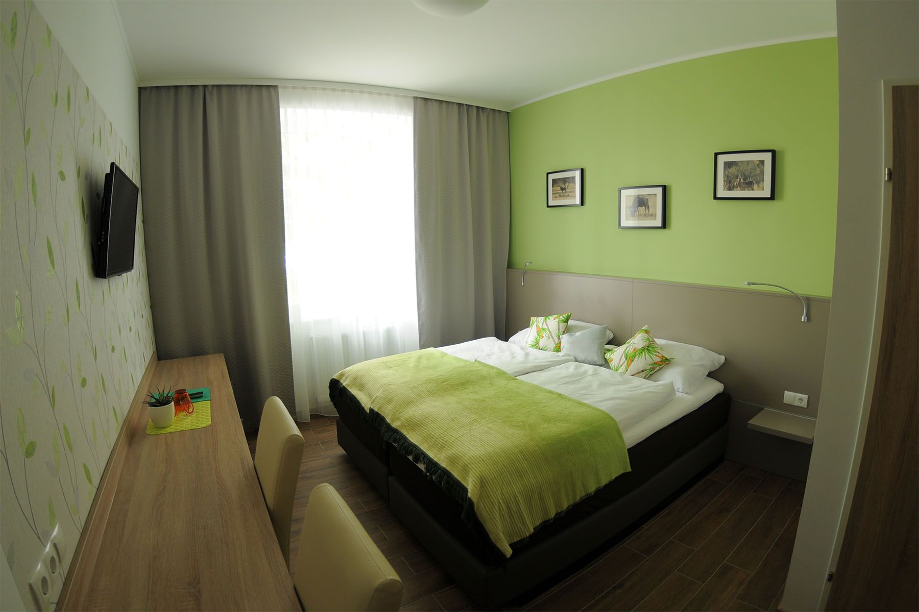 Modernes Gästezimmer mit grünem Farbschema, Doppelbett, Schreibtisch und Wanddekorationen.