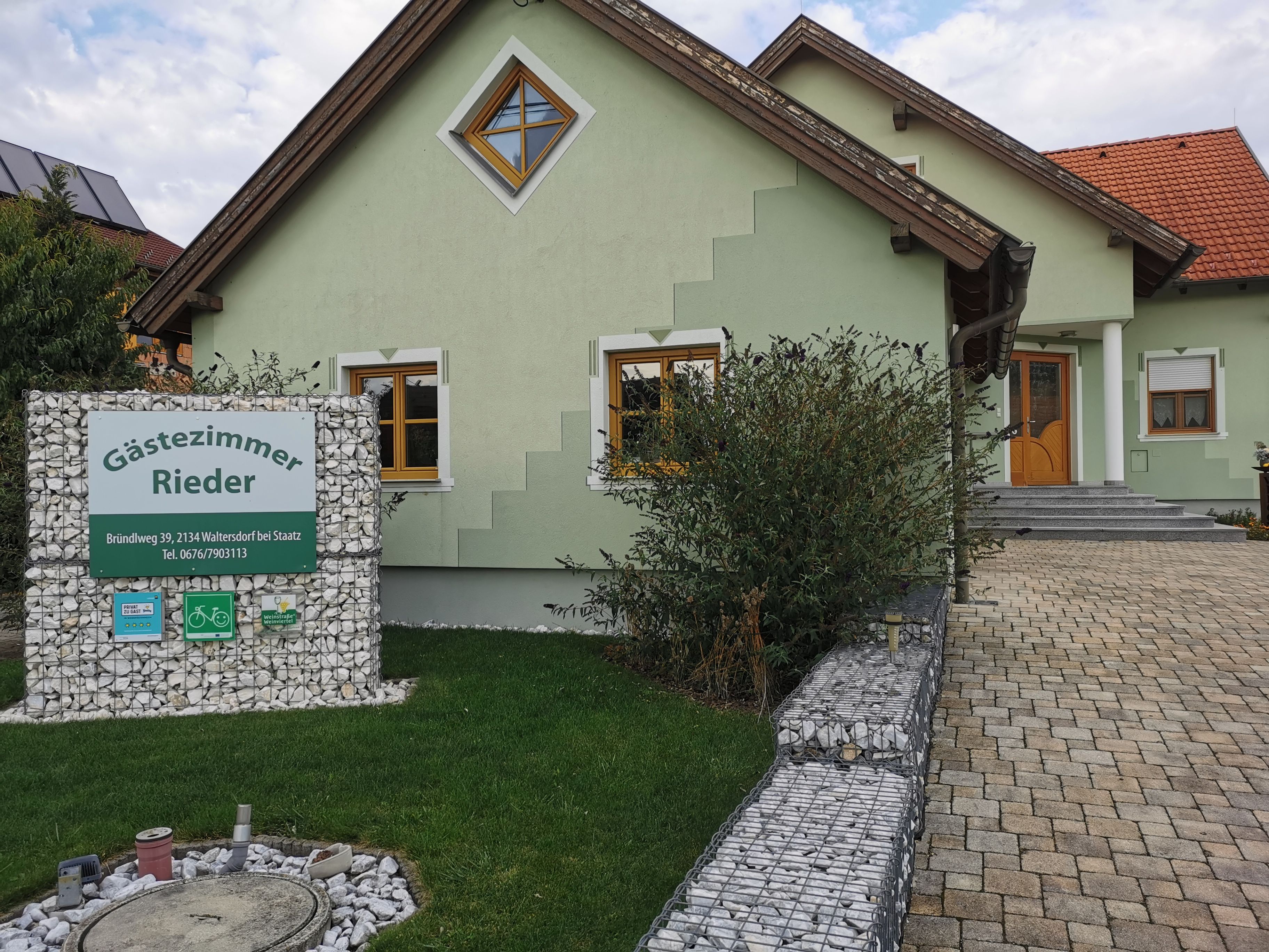 Grünes Haus mit Schild 'Gästezimmer Rieder' im Vorgarten.