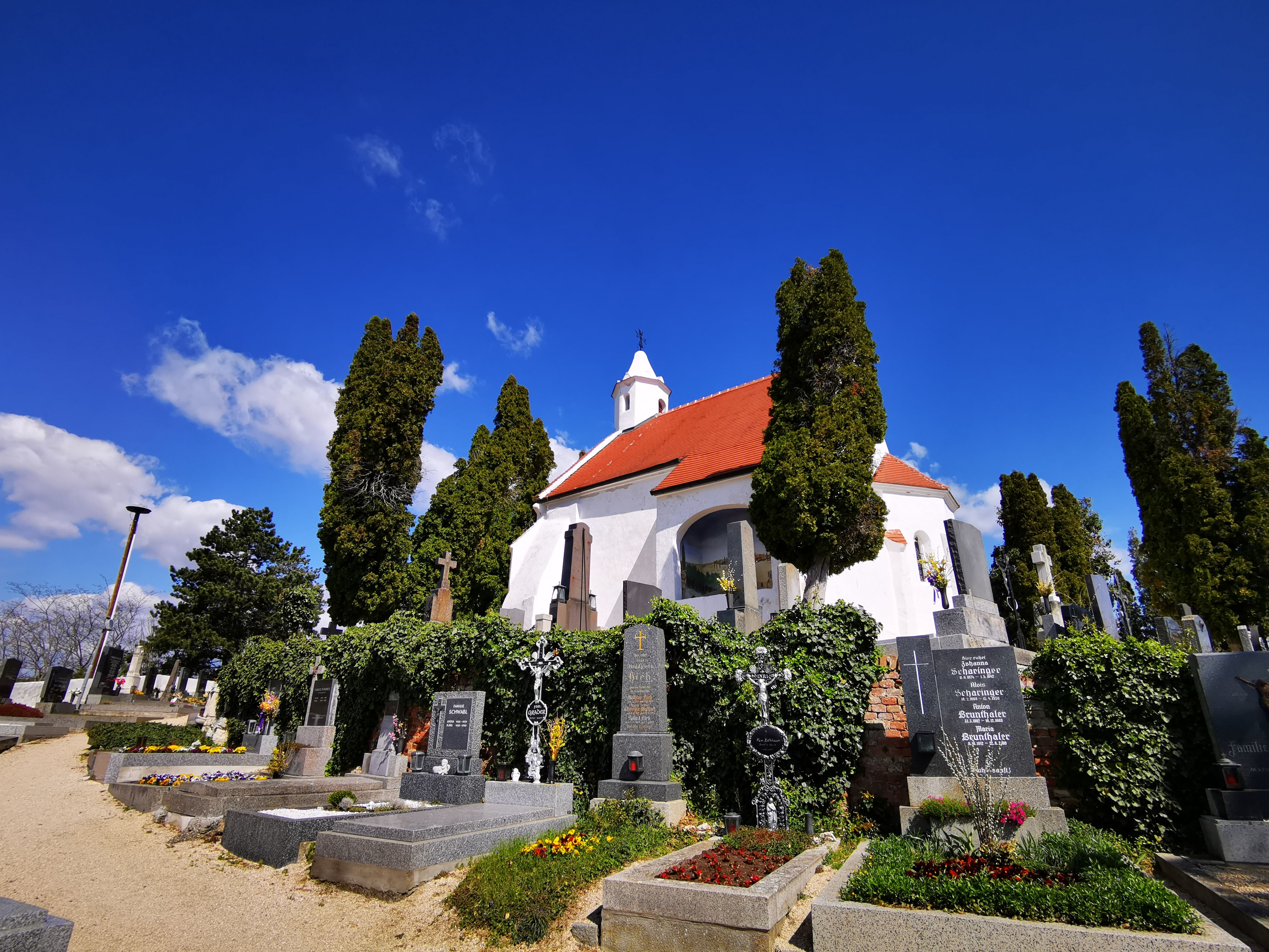 Kunigungenkirche in Mailberg mit Friedhof und blühenden Gräbern im Vordergrund.