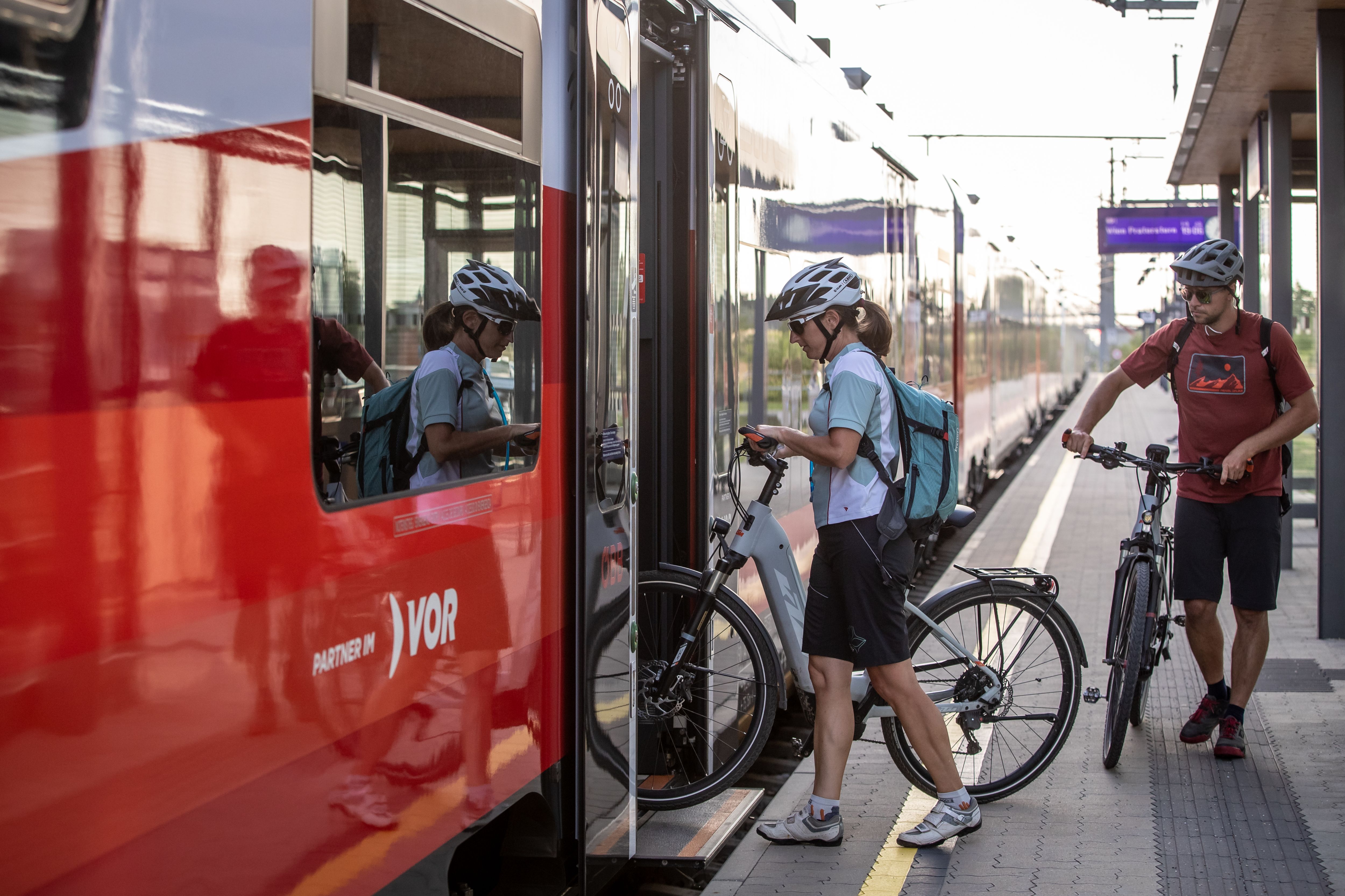Two cyclists get on a train at the station with their bicycles.