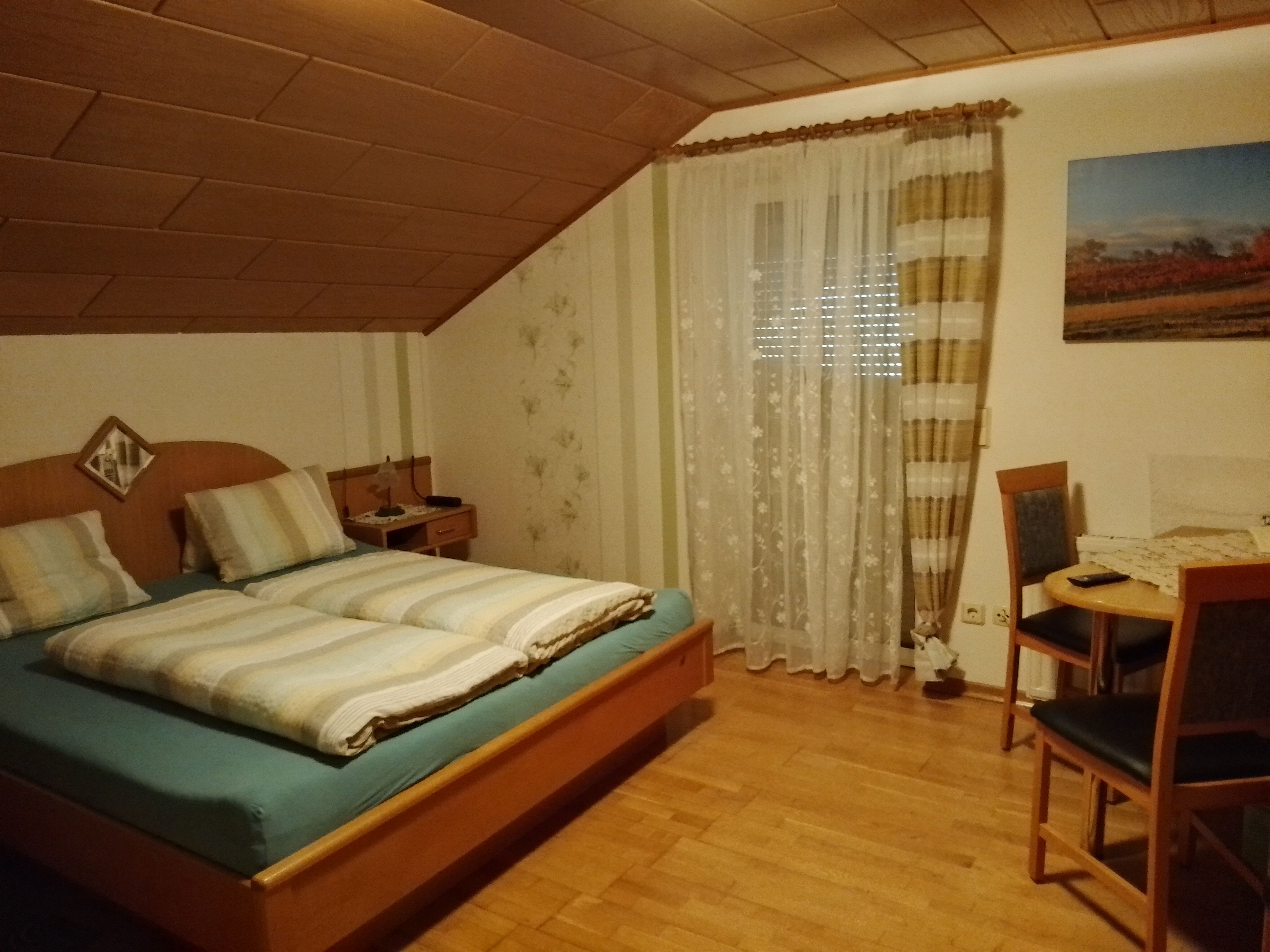 Ein gemütliches Schlafzimmer mit einem Doppelbett, einem kleinen Tisch mit zwei Stühlen und einem Fenster mit Vorhängen.