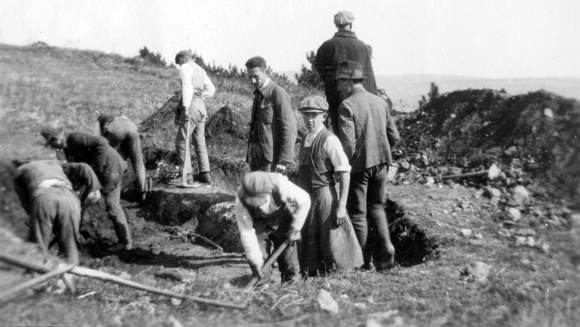 Black and white photo of men digging in a field.
