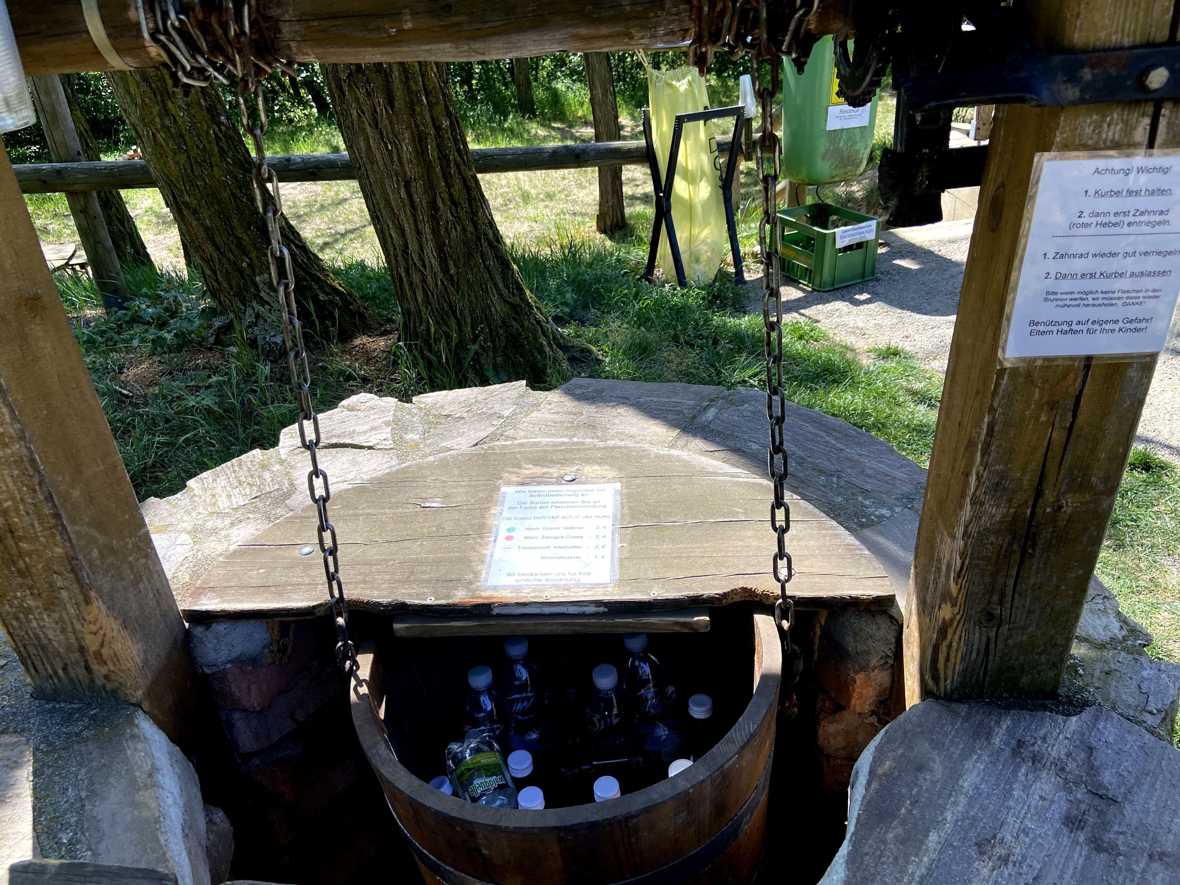 Ein Brunnen mit einer Holzkonstruktion, in dem Flaschen gelagert sind.