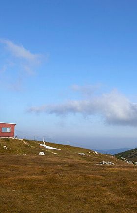 Berghütte steht auf einer Hochebene vor markanter Bergkulisse.