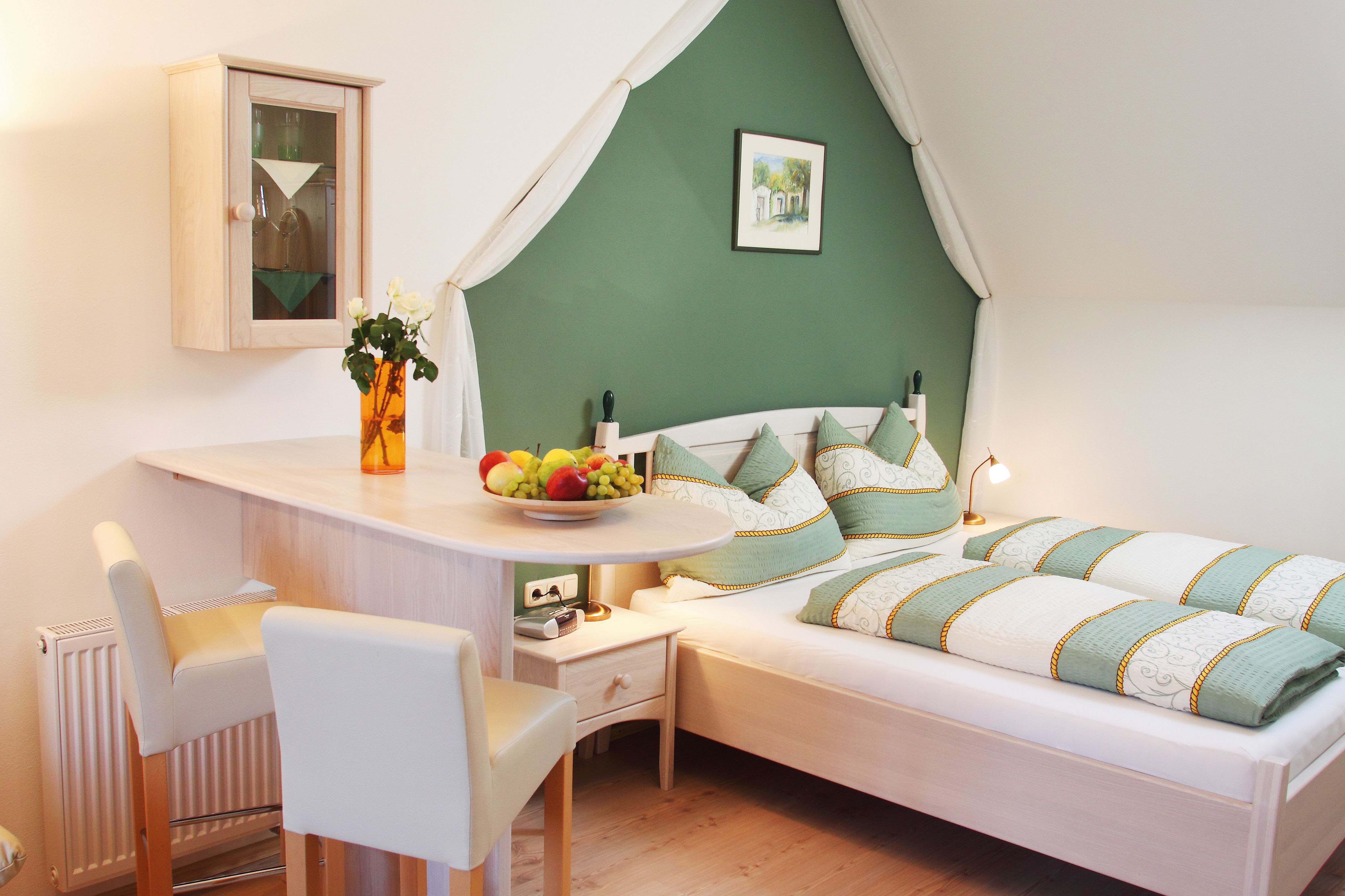 Gemütliches Schlafzimmer mit grün-weißer Bettwäsche, Holzmöbeln und Dekorationen.