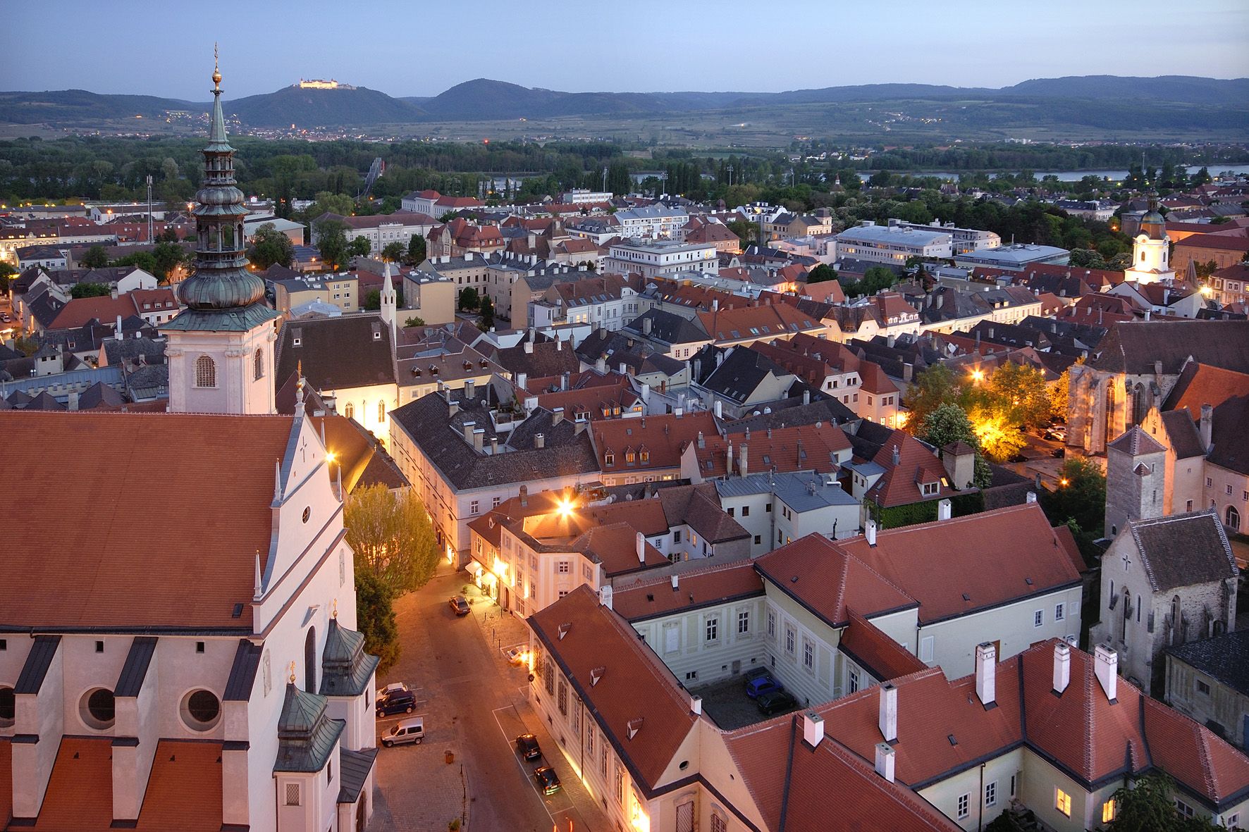 Abendliche Stadtansicht von Krems mit beleuchteten Gebäuden und Hügeln im Hintergrund.