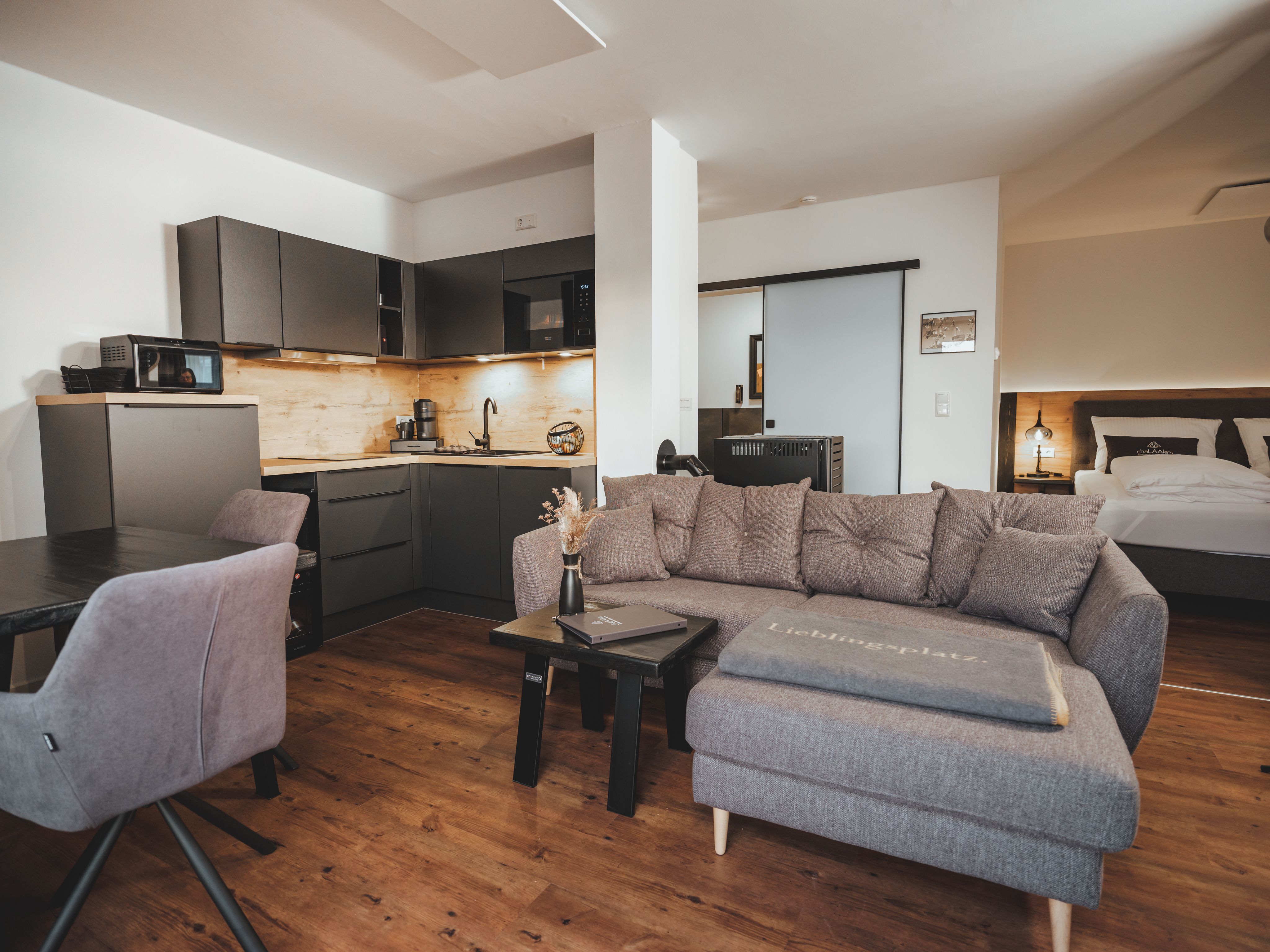 Moderner Wohnbereich mit grauem Sofa, Küchenzeile und Esstisch.