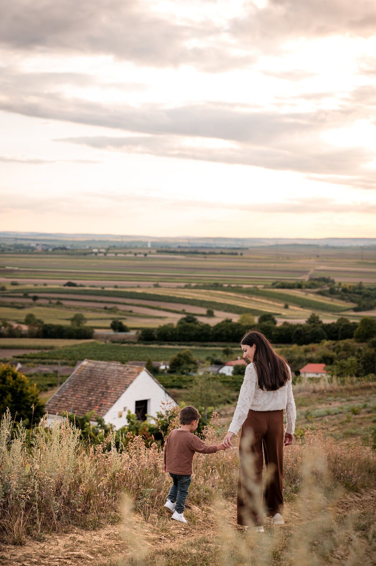 Eine Mutter spaziert mit ihrem Sohn vorbei an einem Presshaus durch die Weinviertler Landschaft - mit weitem Ausblick über die sanften Hügel der Region. 