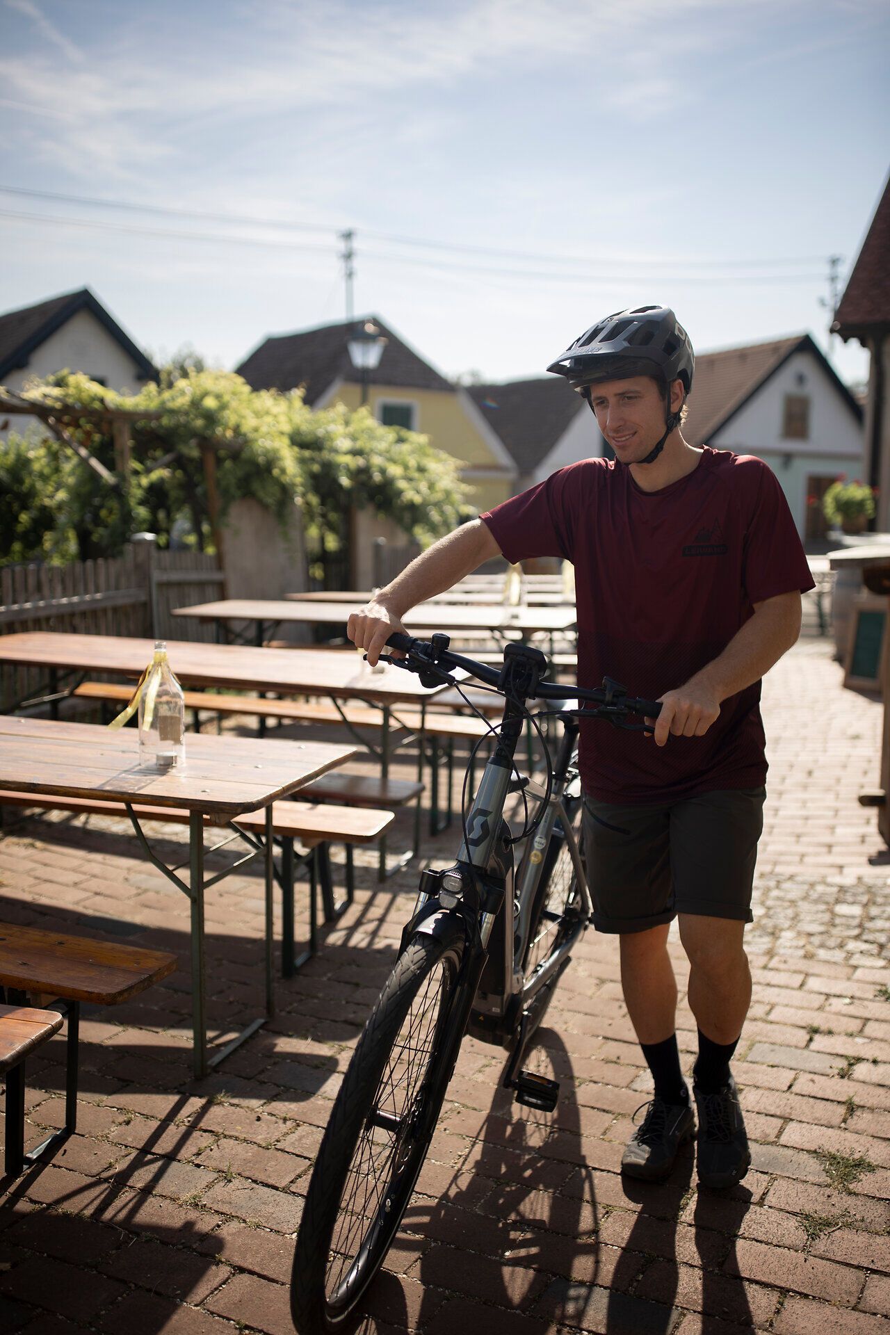 Ein junger Radfahrer genießt die warmen Sonnenstrahlen, während er durch die charmante Kellergasse Oagossn radelt. Umgeben von malerischen Weinbergen und rustikalen Holzhütten, vermittelt die Szenerie ein Gefühl von Freiheit und Abenteuer. Hier in der idyllischen Landschaft des Weinviertels wird jeder Moment zum unvergesslichen Erlebnis.