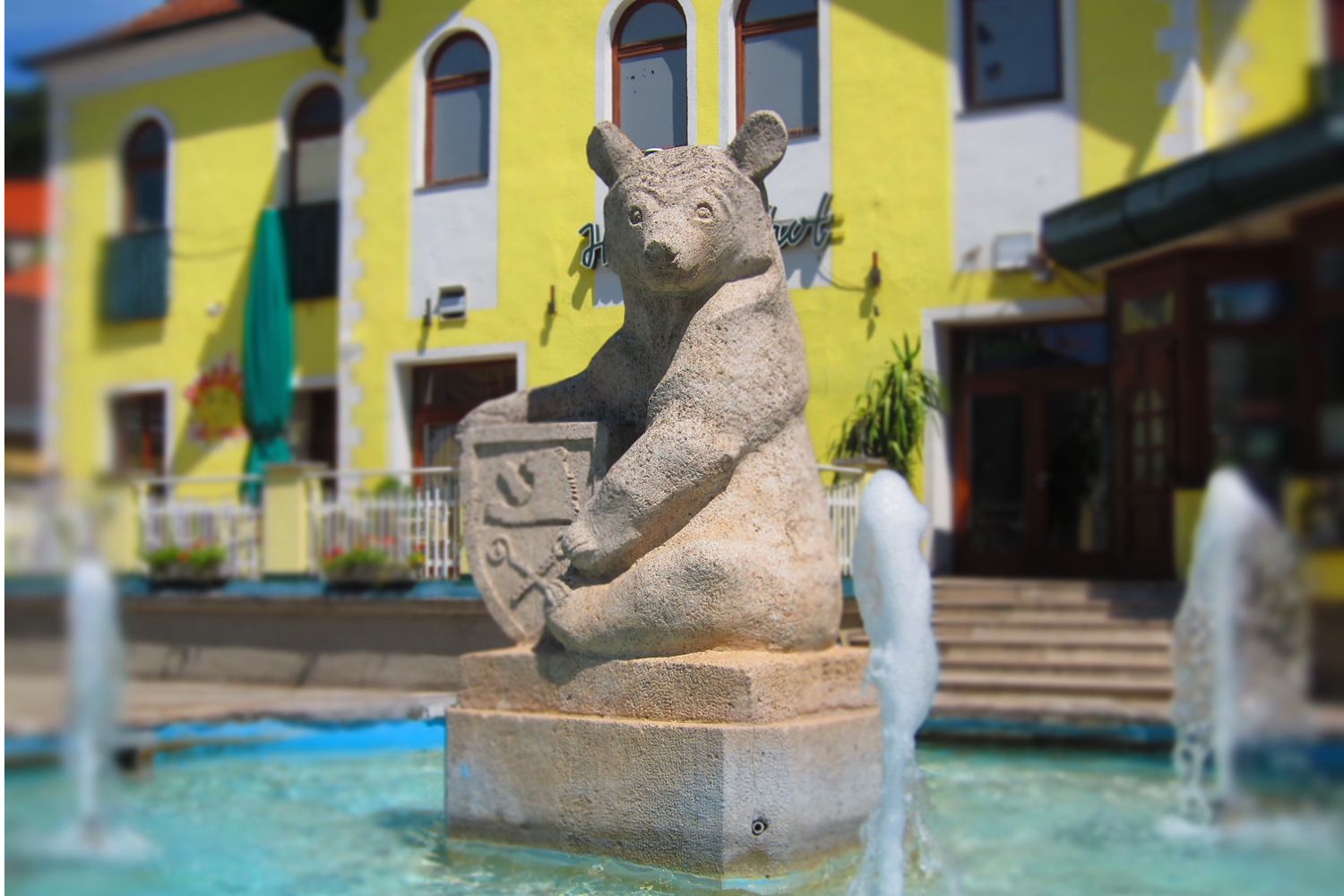 Steinbär-Skulptur mit Wappen in einem Brunnen vor einem gelben Gebäude.