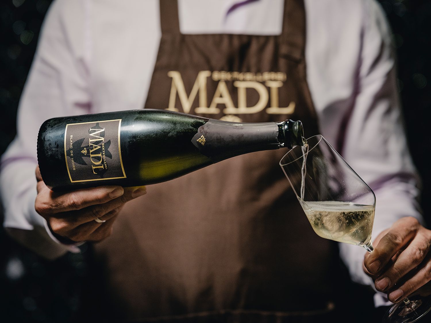 Person schenkt Sekt aus einer Madl-Flasche in ein Glas ein.