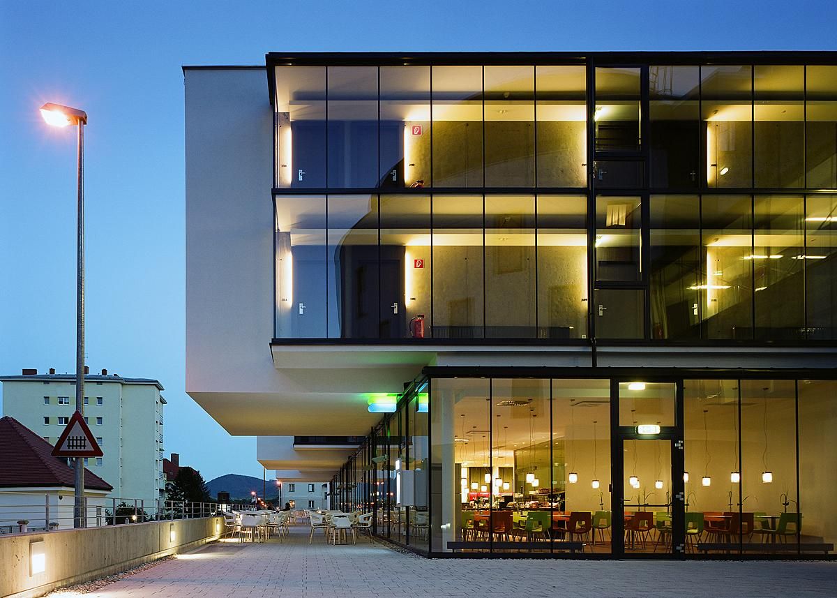 Modernes Hotelgebäude mit Glasfassade bei Dämmerung, beleuchtete Innenräume sichtbar.