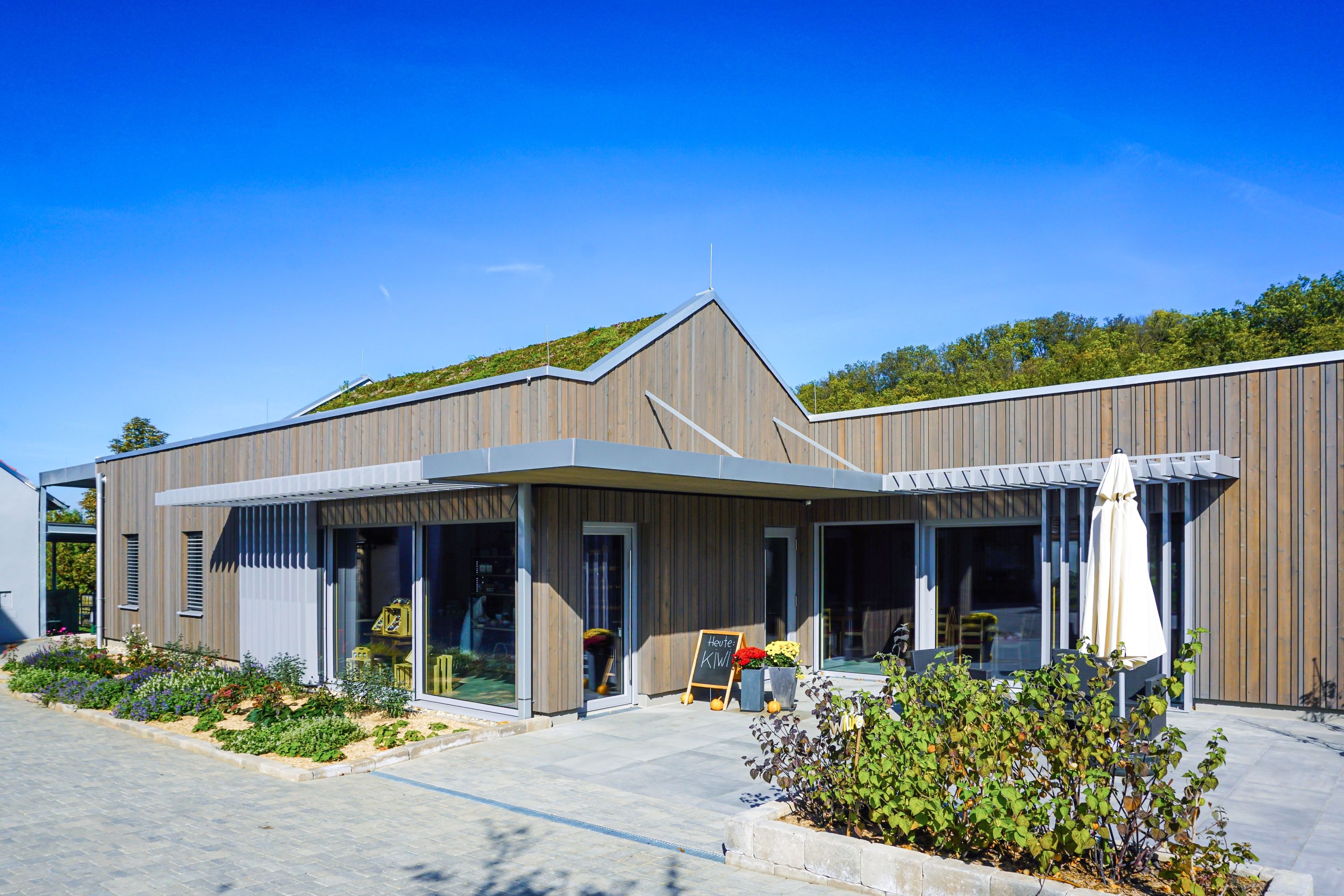 Modernes Gebäude mit Holzverkleidung und begrüntem Dach bei sonnigem Wetter.