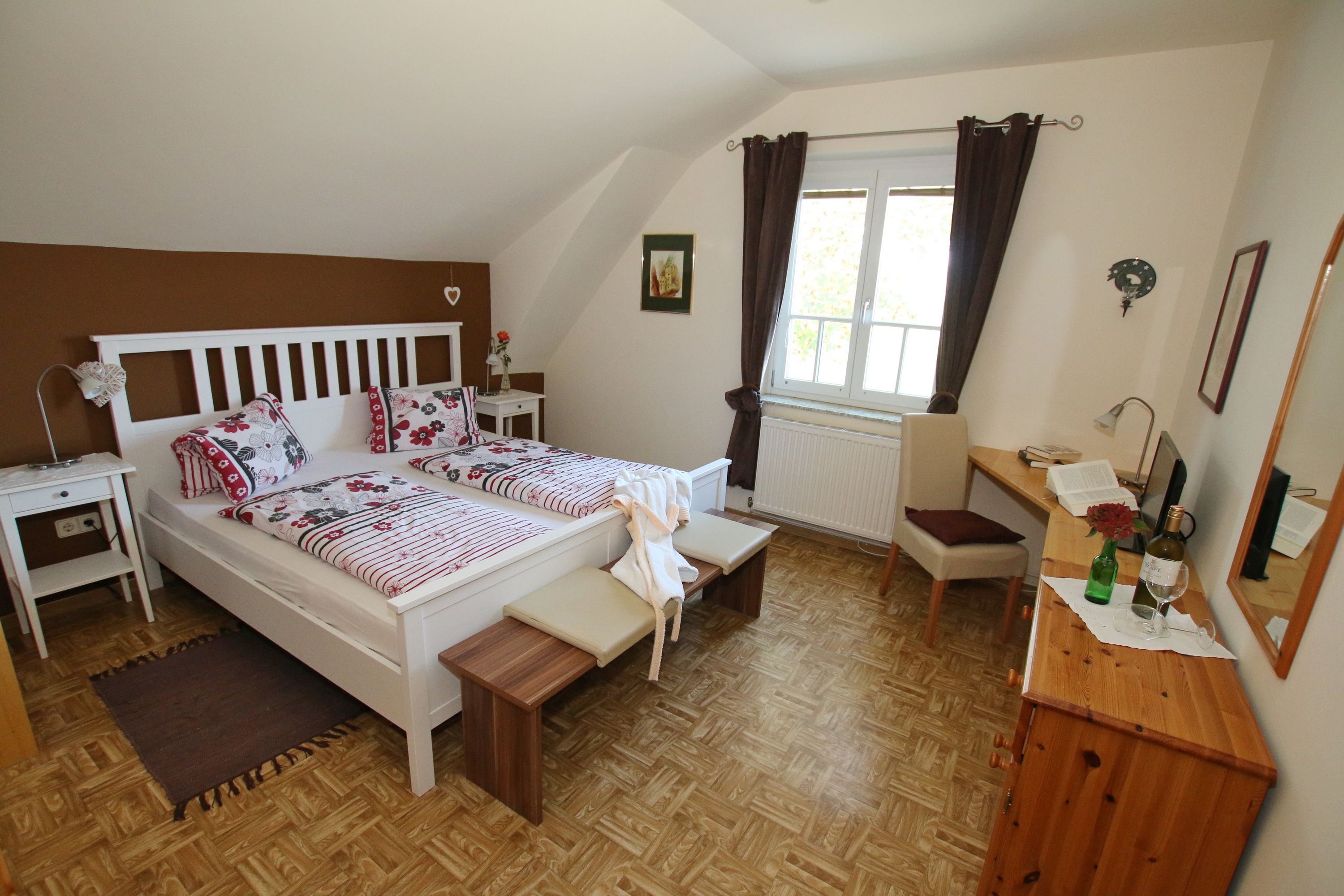 Gemütliches Gästezimmer mit Doppelbett, Sofa, Tisch und Stuhl. Braune Akzentwand und dunkle Vorhänge.