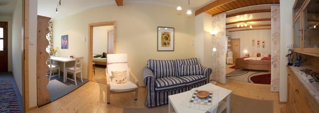 Panorama eines gemütlichen Wohnzimmers mit Sofa, Esstisch und Schlafzimmer im Hintergrund.