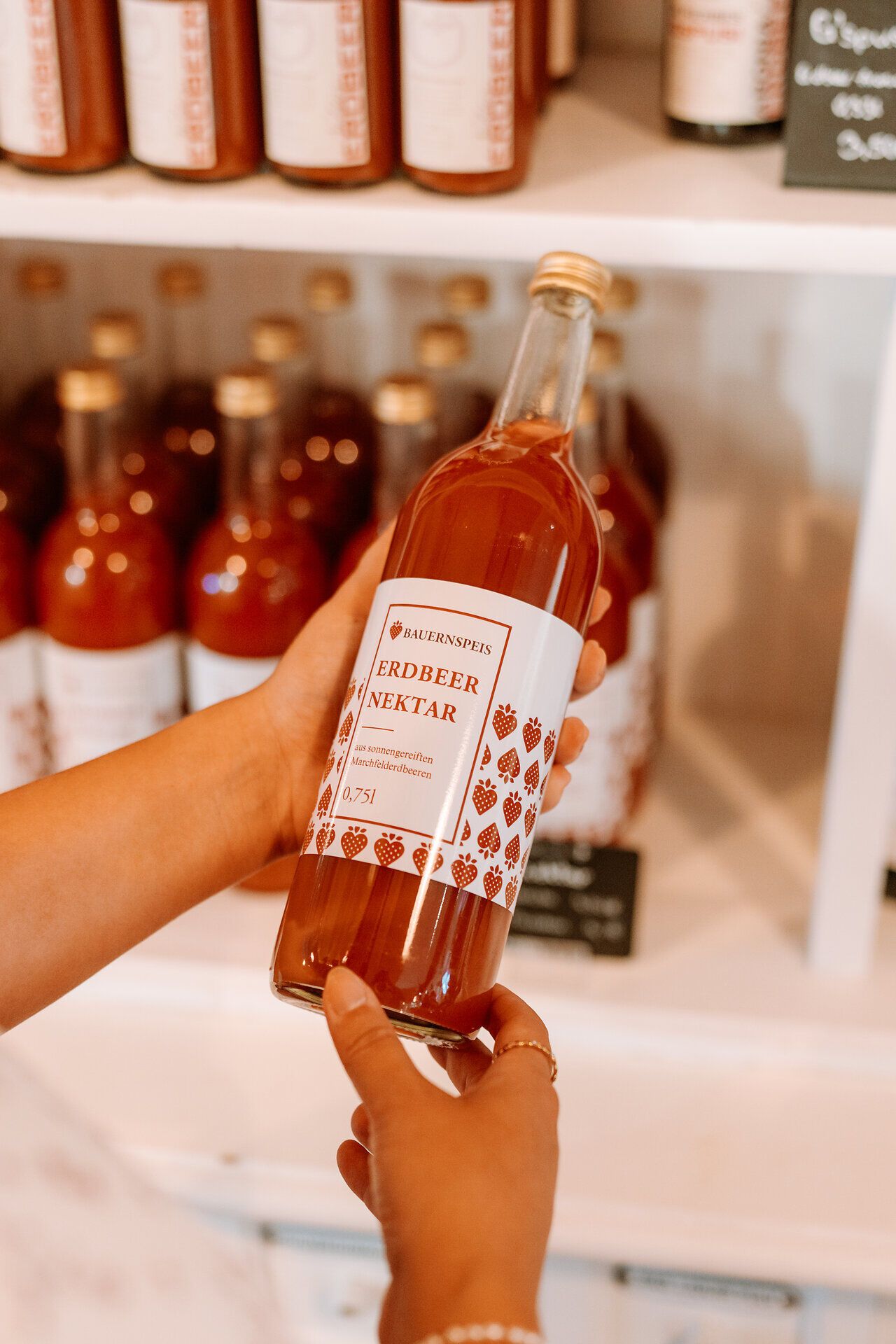 In einem einladenden Hofladen wird ein köstlicher Erdbeernektar präsentiert, der die frischen Aromen des Marchfelds verkörpert. Die liebevoll gestaltete Flasche verspricht Genuss und regionale Qualität, ideal für ein erfrischendes Frühstück oder einen gemütlichen Nachmittag.