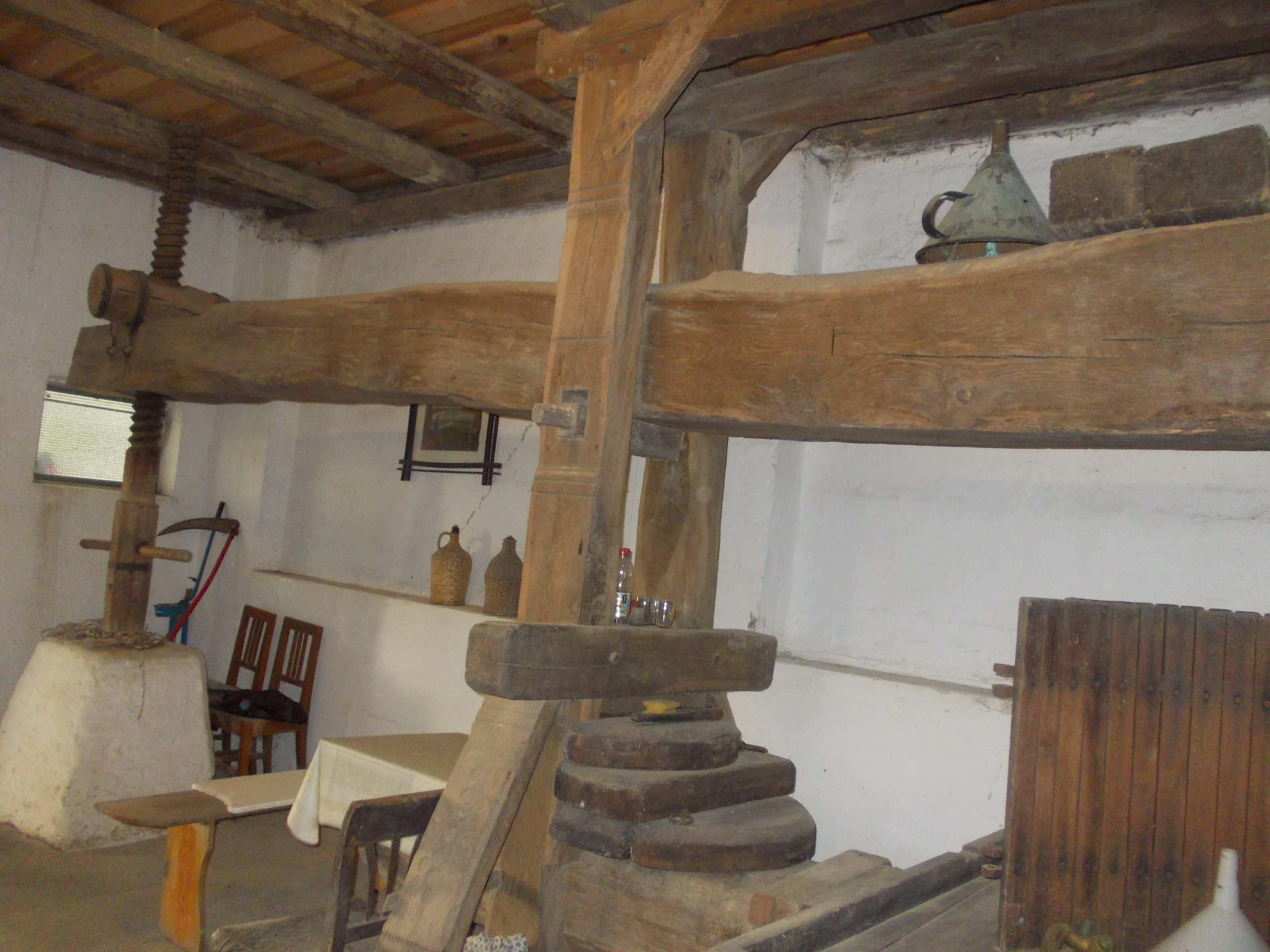 Alte Weinpresse in einem rustikalen Raum mit Holzbalken und antiken Gegenständen.