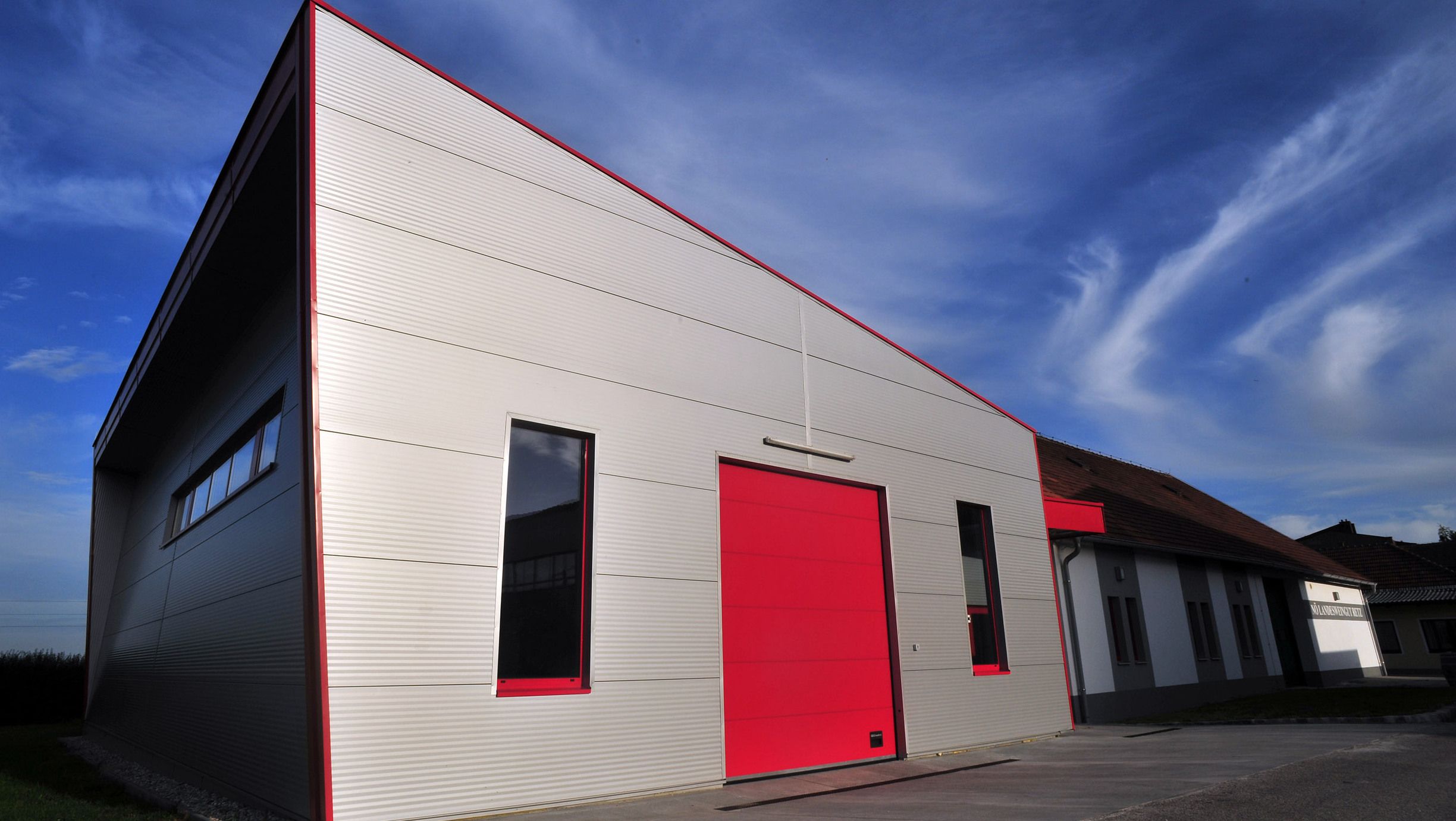 Modernes Gebäude mit rotem Tor und blauer Himmel im Hintergrund.