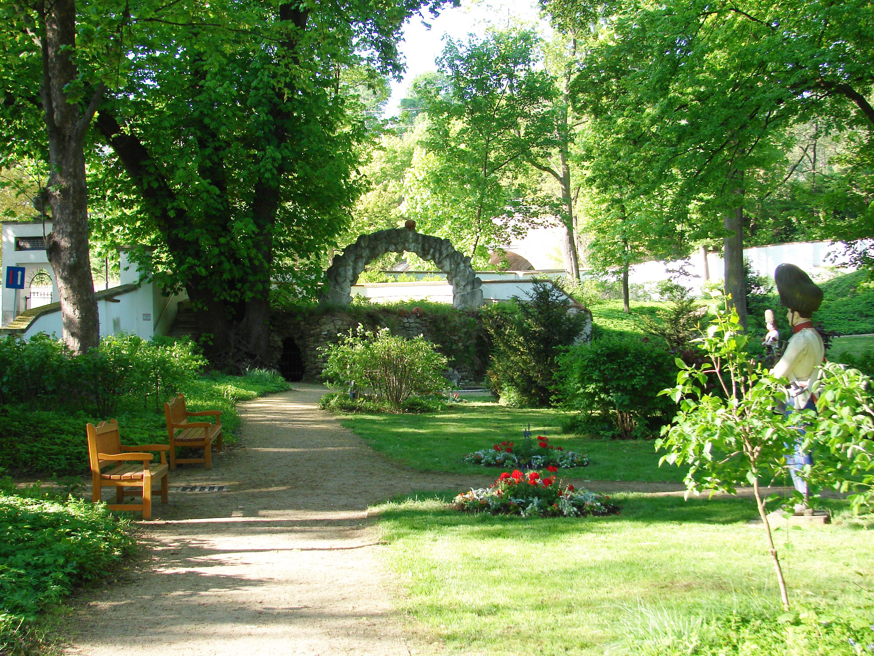 Ein grüner Garten mit Bäumen, Bänken und einer Statue.