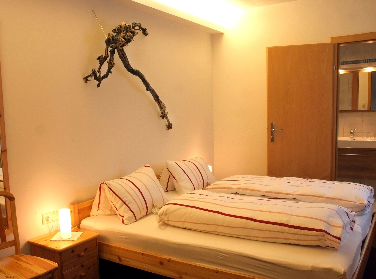 Gemütliches Schlafzimmer mit Doppelbett, Nachttischlampe und Weinstock-Dekoration an der Wand.